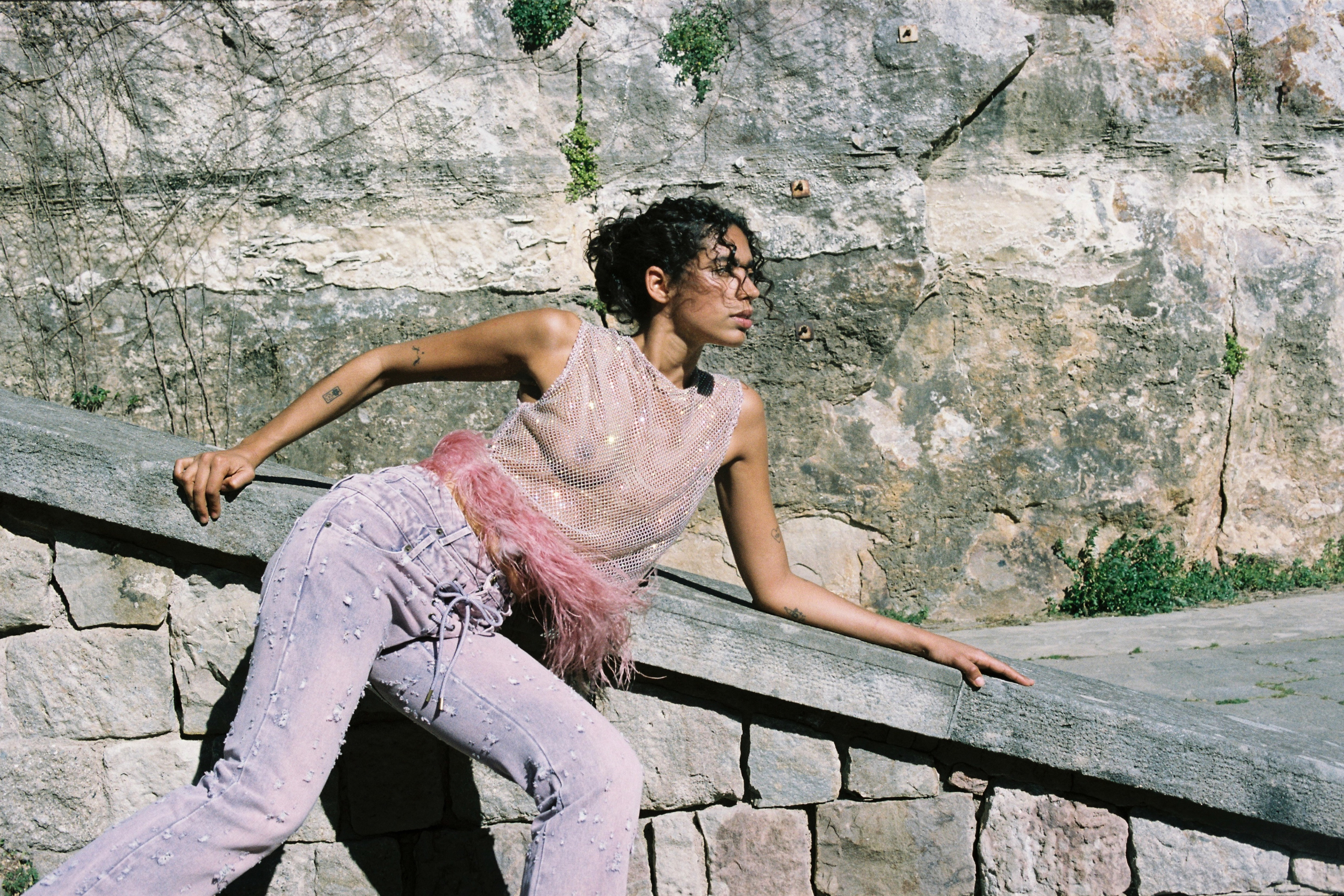 Fashionable person posing against a rustic stone wall in stylish outfit.