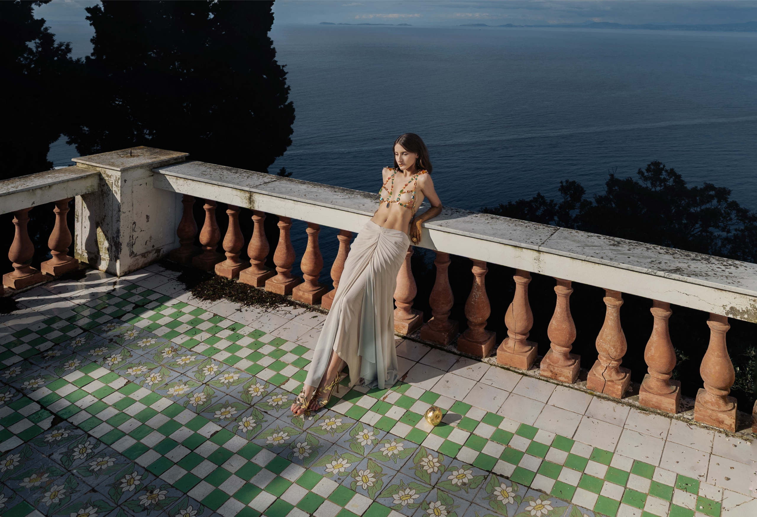 Woman in elegant outfit on a terrace overlooking the ocean with tiled floor.