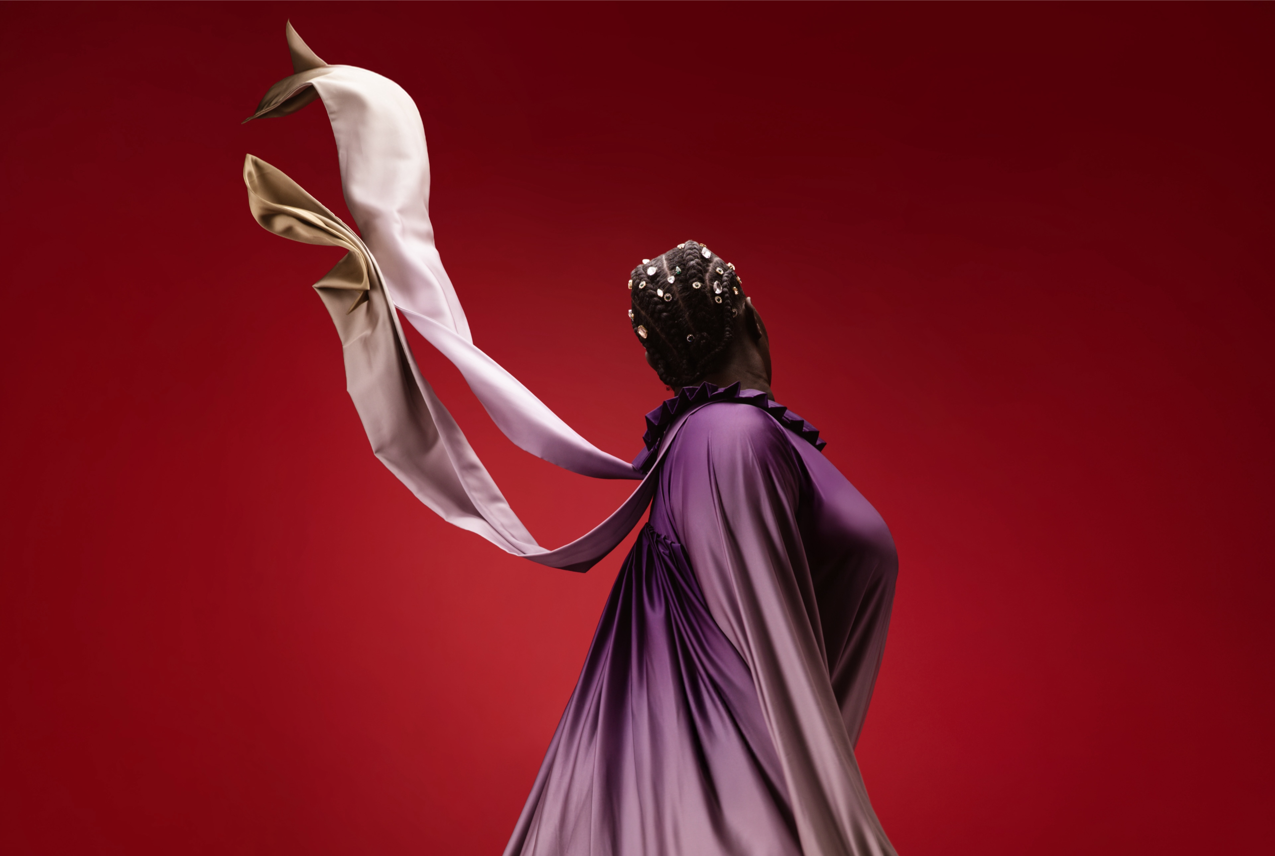 Purple gown with flowing ribbons against red background. Fashion and elegance in motion.