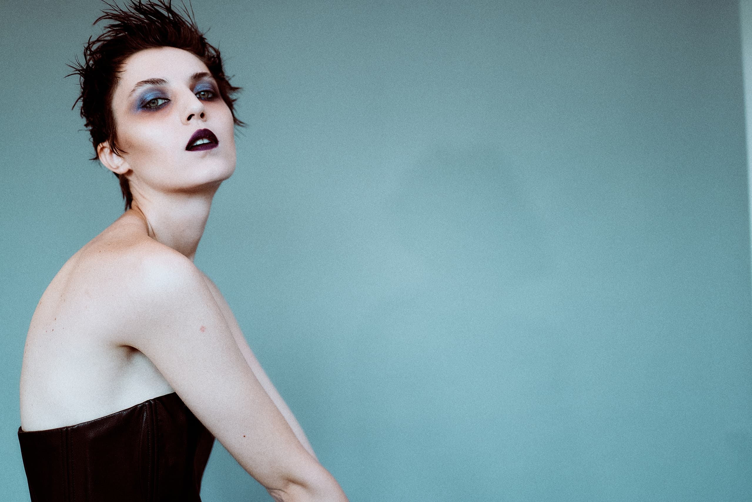 Fashion model with bold makeup and short hair against a blue background.