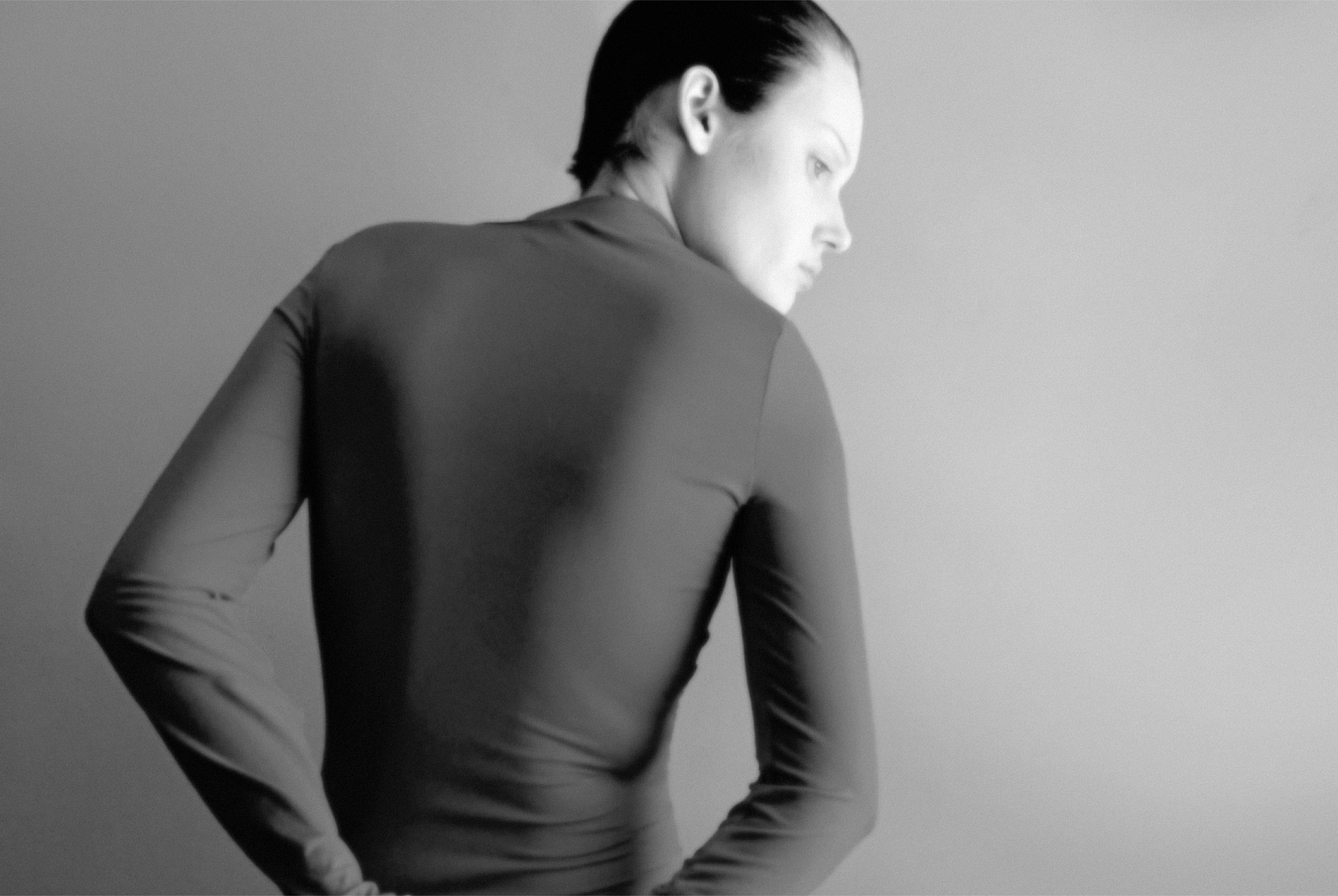 Monochrome image of a person in a fitted top, facing away, gazing thoughtfully.