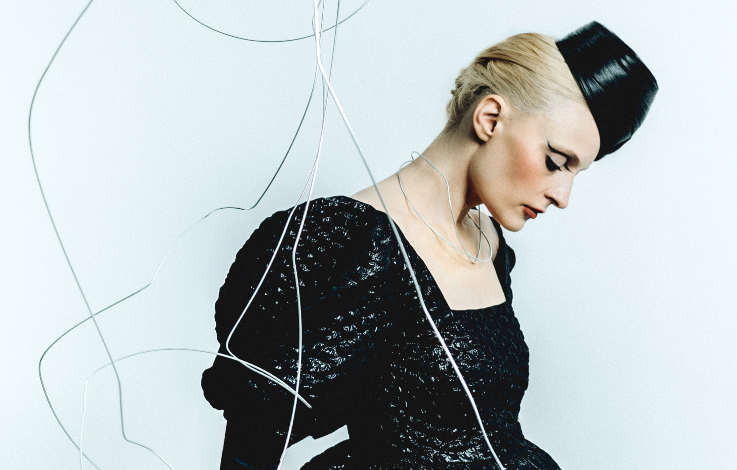 Elegant woman in black avant-garde fashion with cables surrounding her.