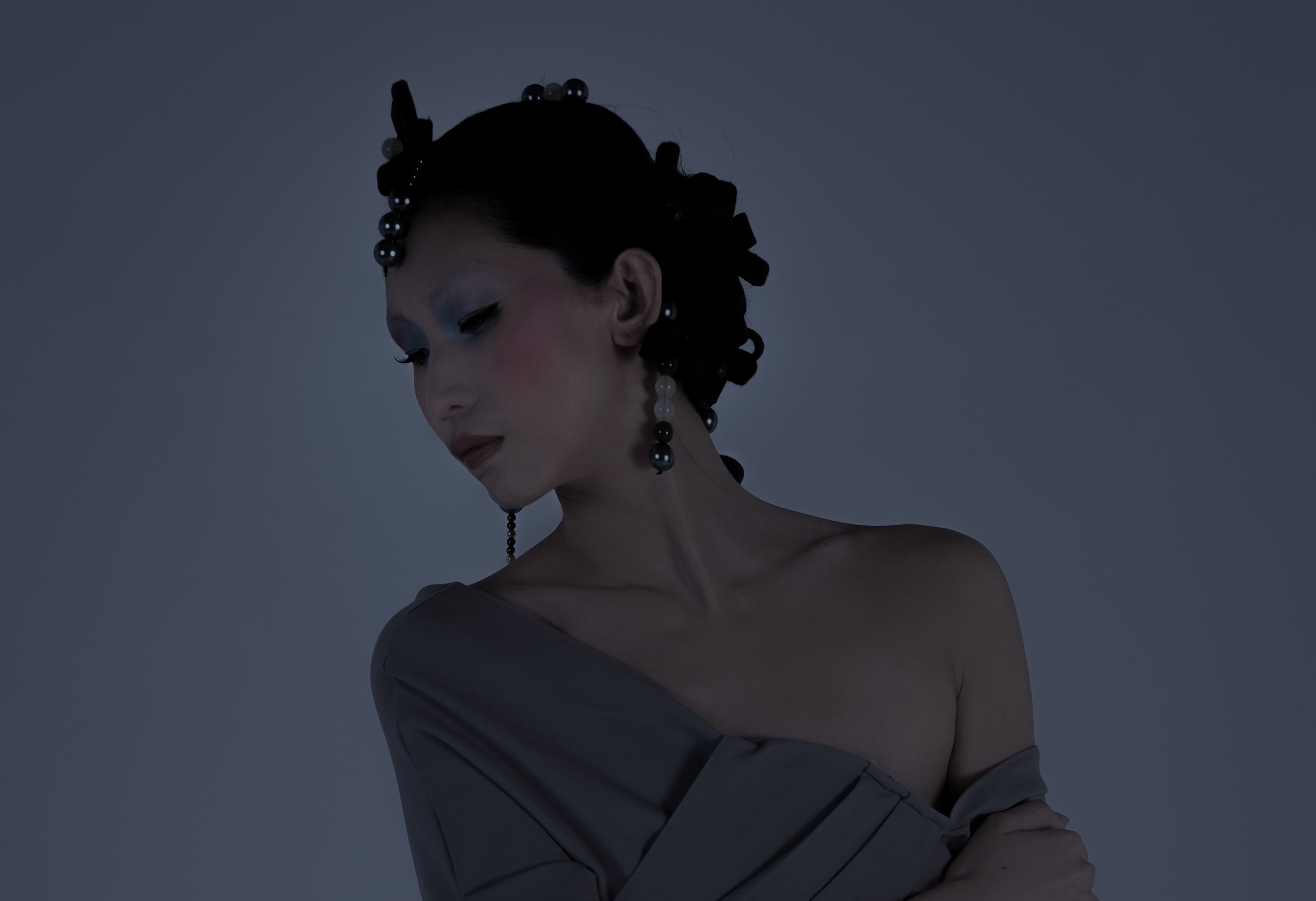 Elegant woman with artistic hairstyle and soft makeup, gazing downwards.