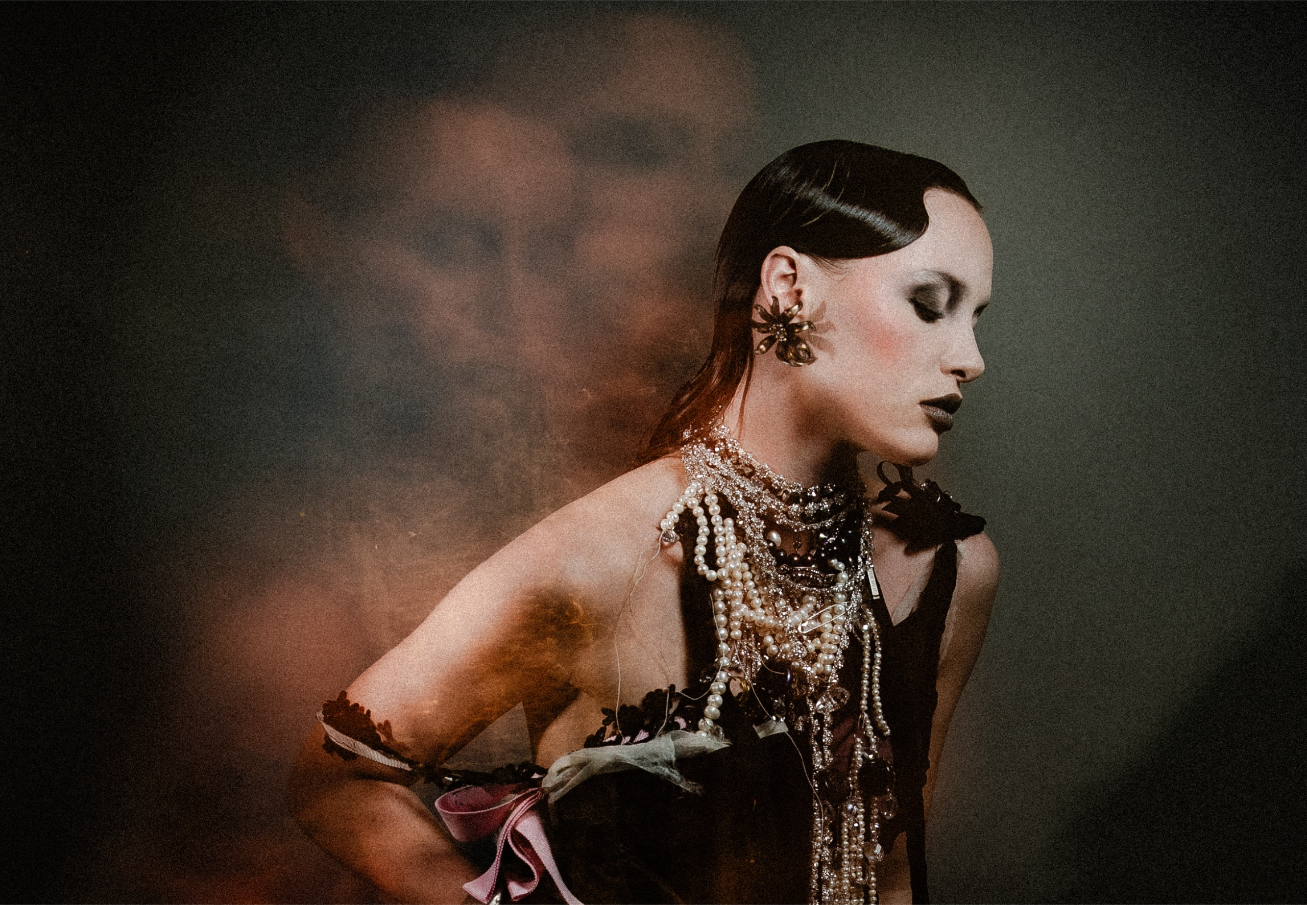 Elegant woman in dark artsy fashion, adorned with pearls against a mysterious background.