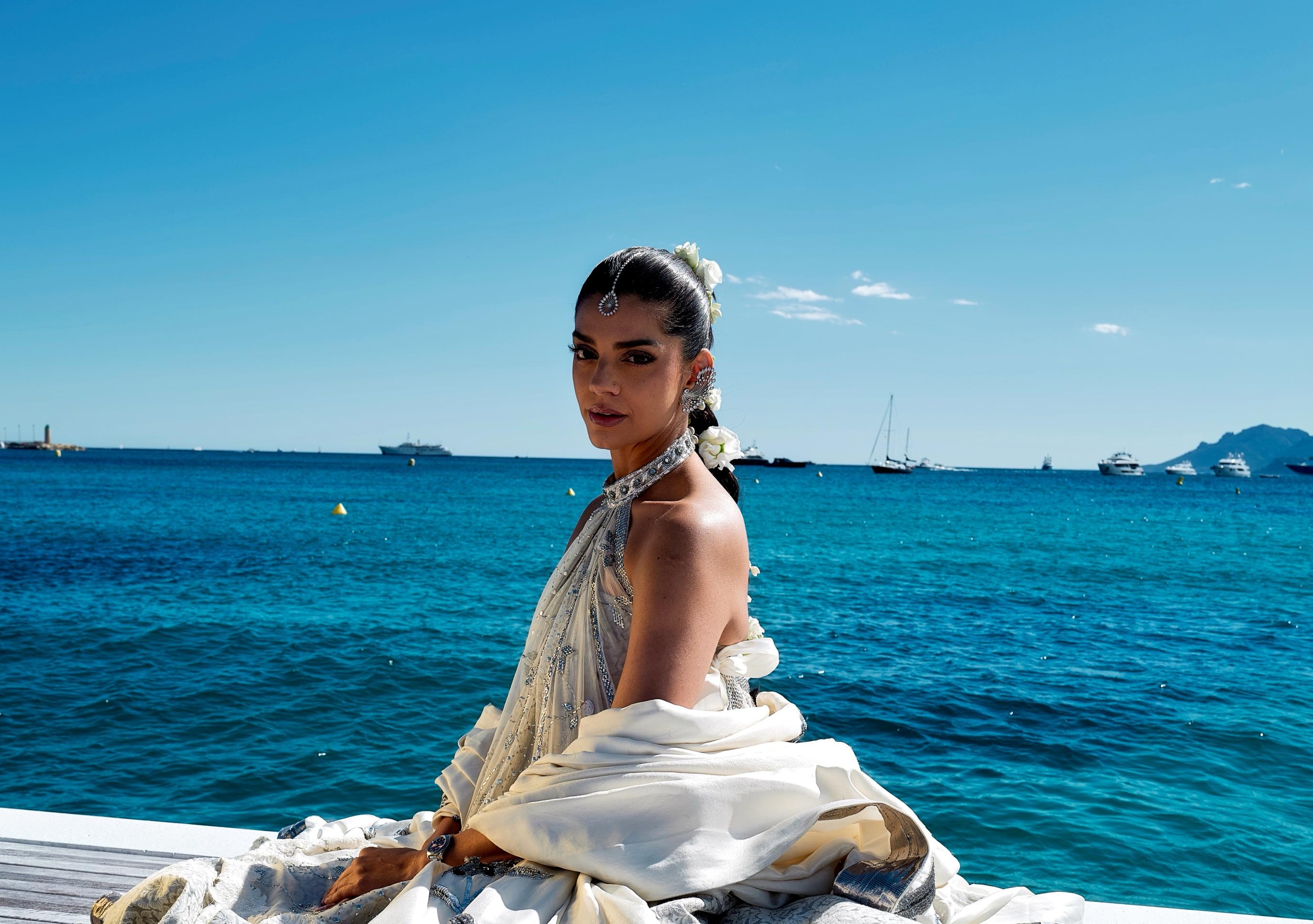 Elegant woman in white by the sea with yachts in the background.