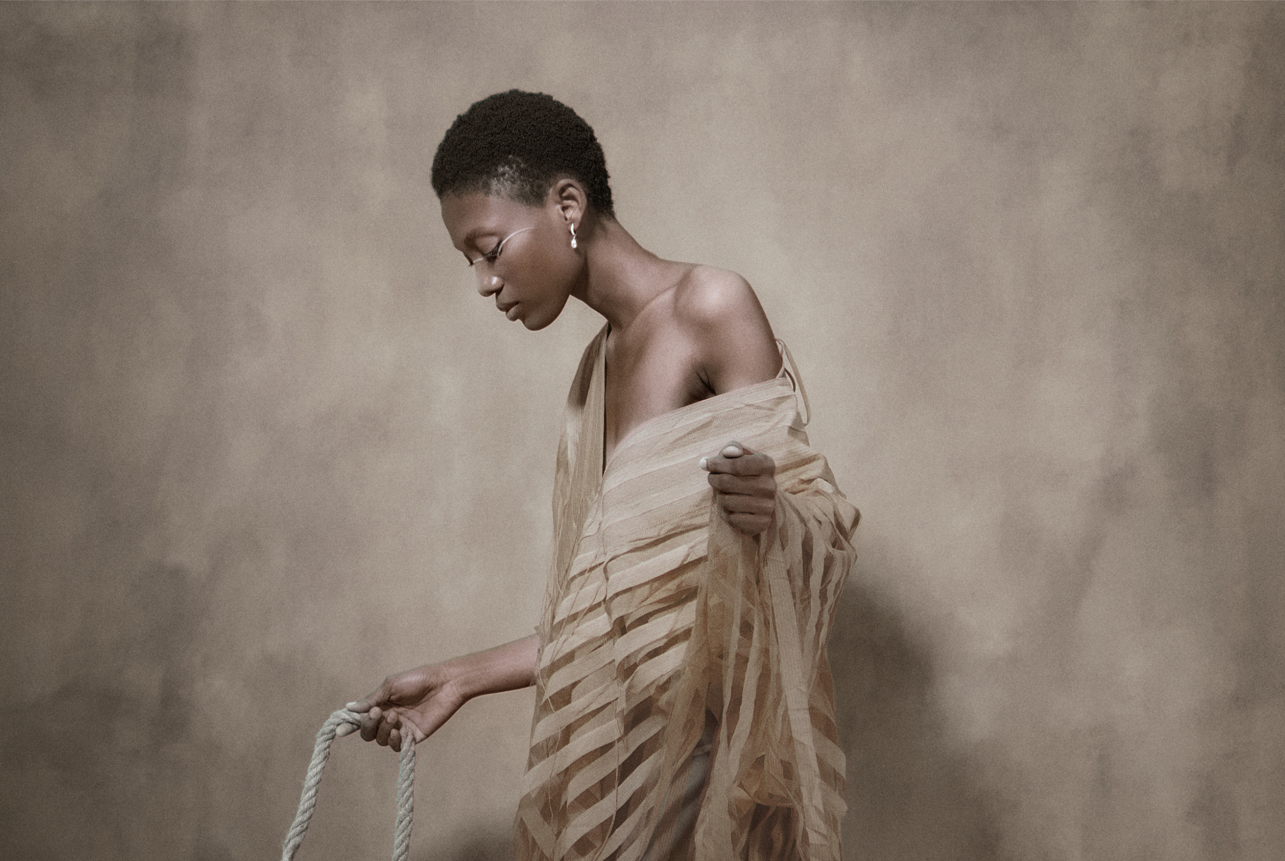 Elegant woman draped in sheer fabric holding a rope, side profile.