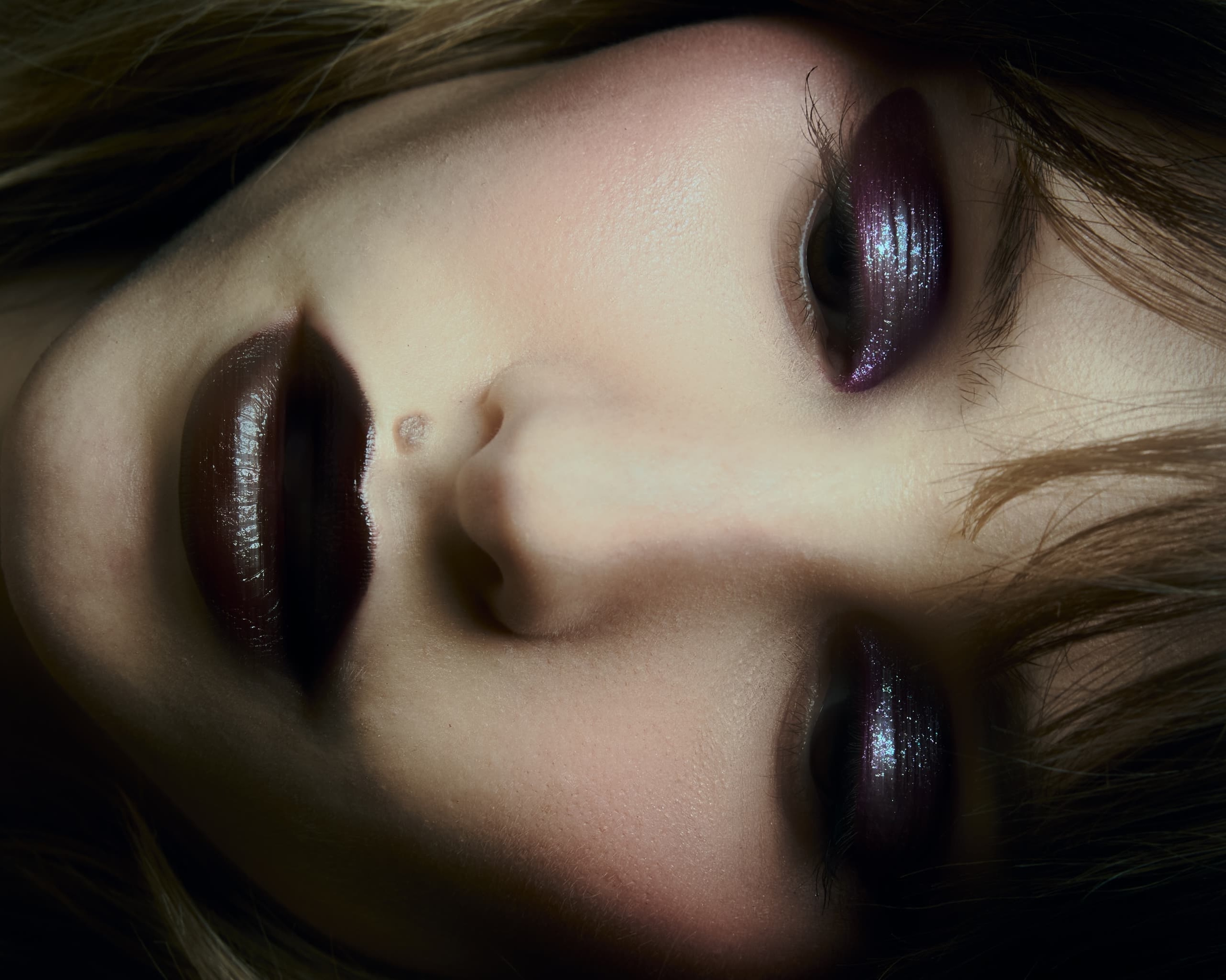 Close-up of woman with dark lips and shimmering purple eye makeup.