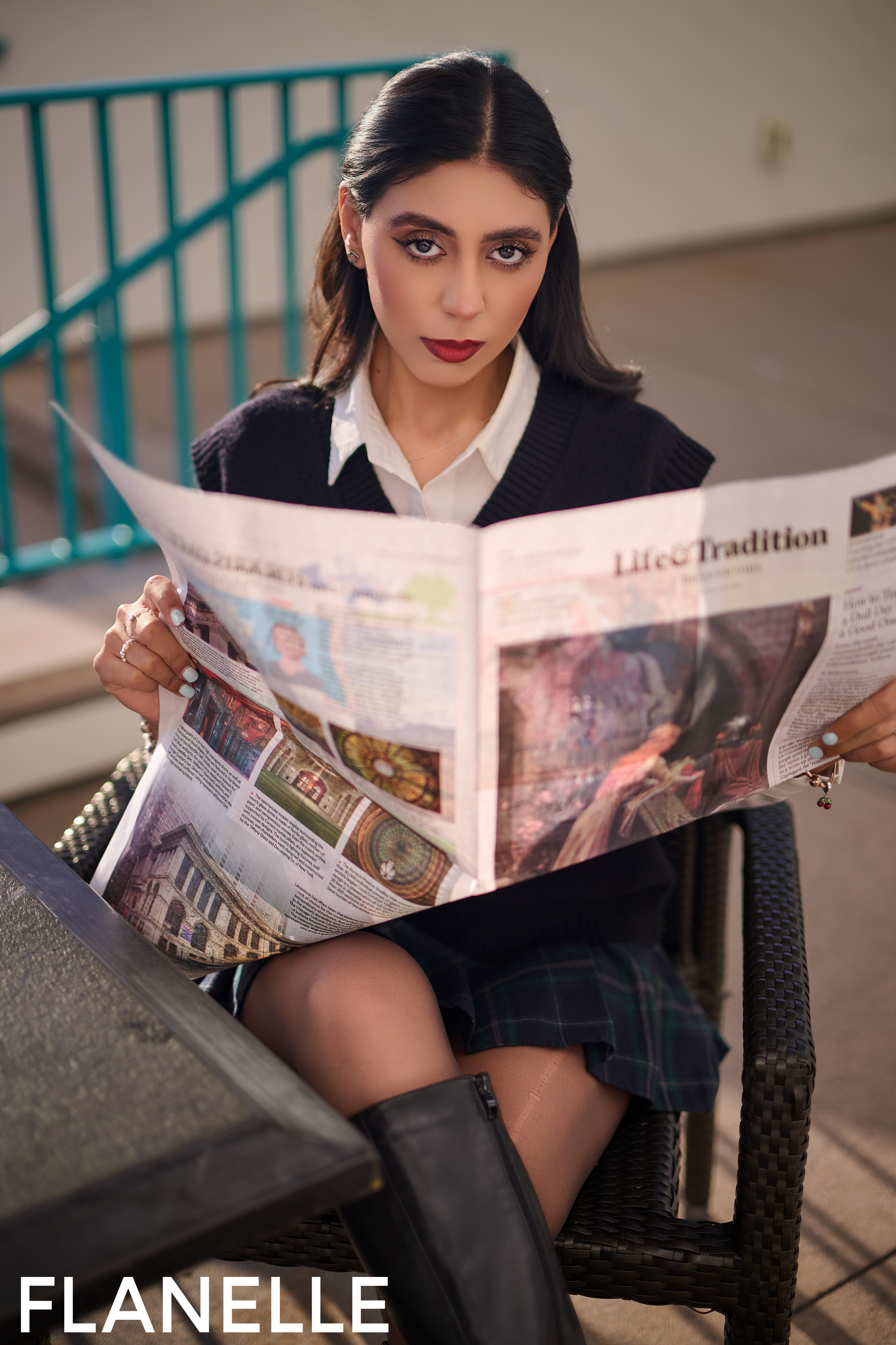 Woman reading a newspaper outdoors, wearing black sweater and boots.