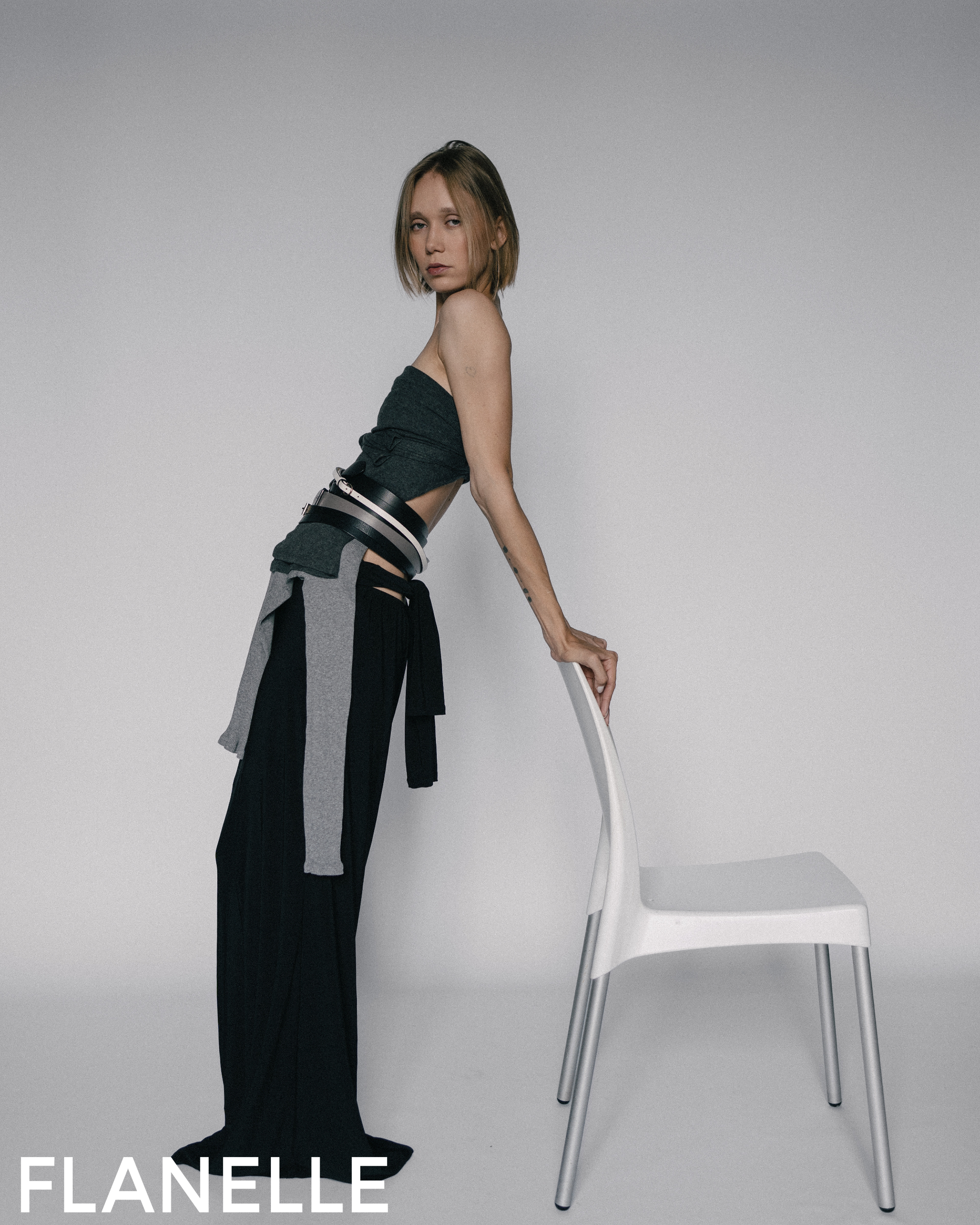 Fashion model in stylish outfit posing with a chair in a minimalist setting.