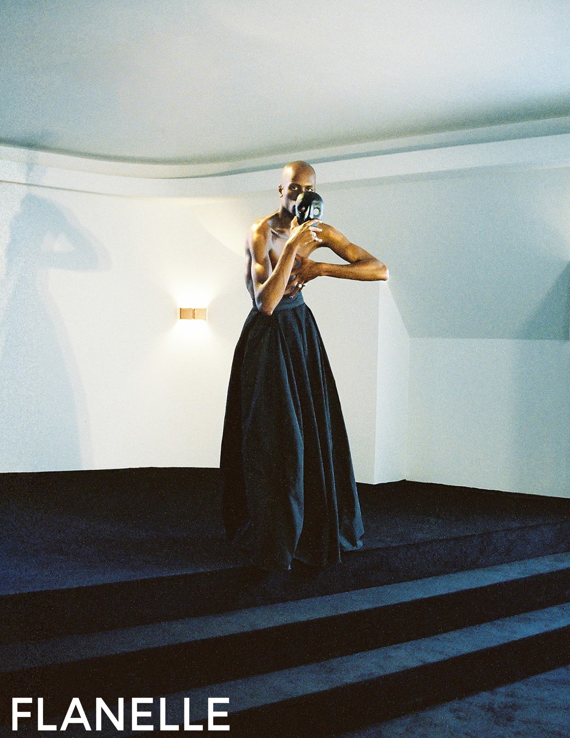 Person in a long skirt holding a mask on a dimly lit staircase.