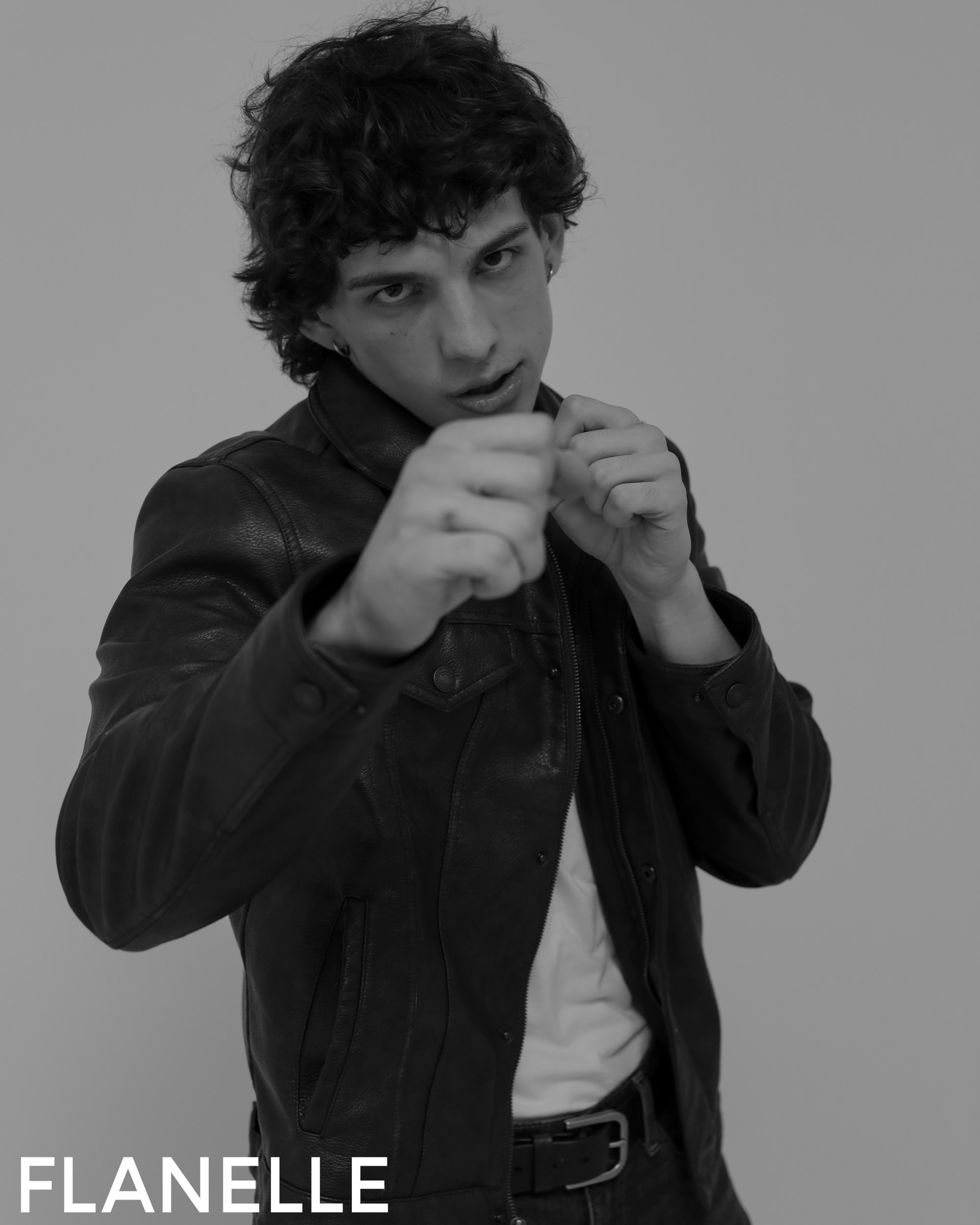 Person striking a pose in leather jacket, black and white photo.