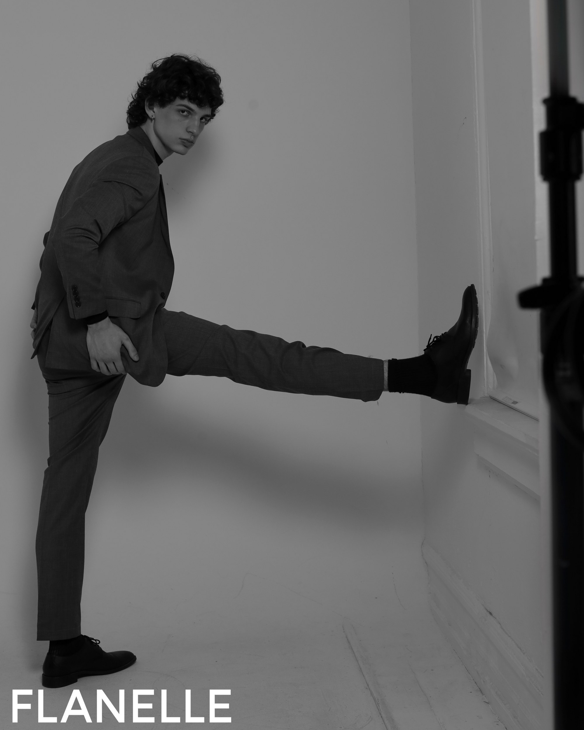 Man in suit kicking leg up in stylish black and white photoshoot.