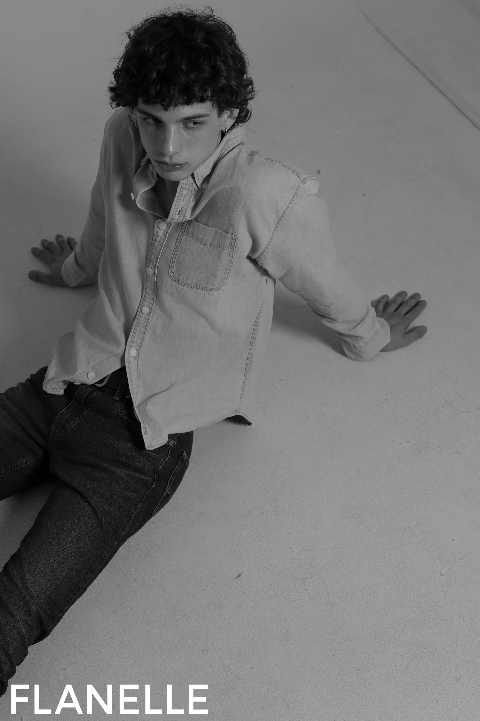 Man in casual outfit sitting on floor, wearing a flannel shirt.