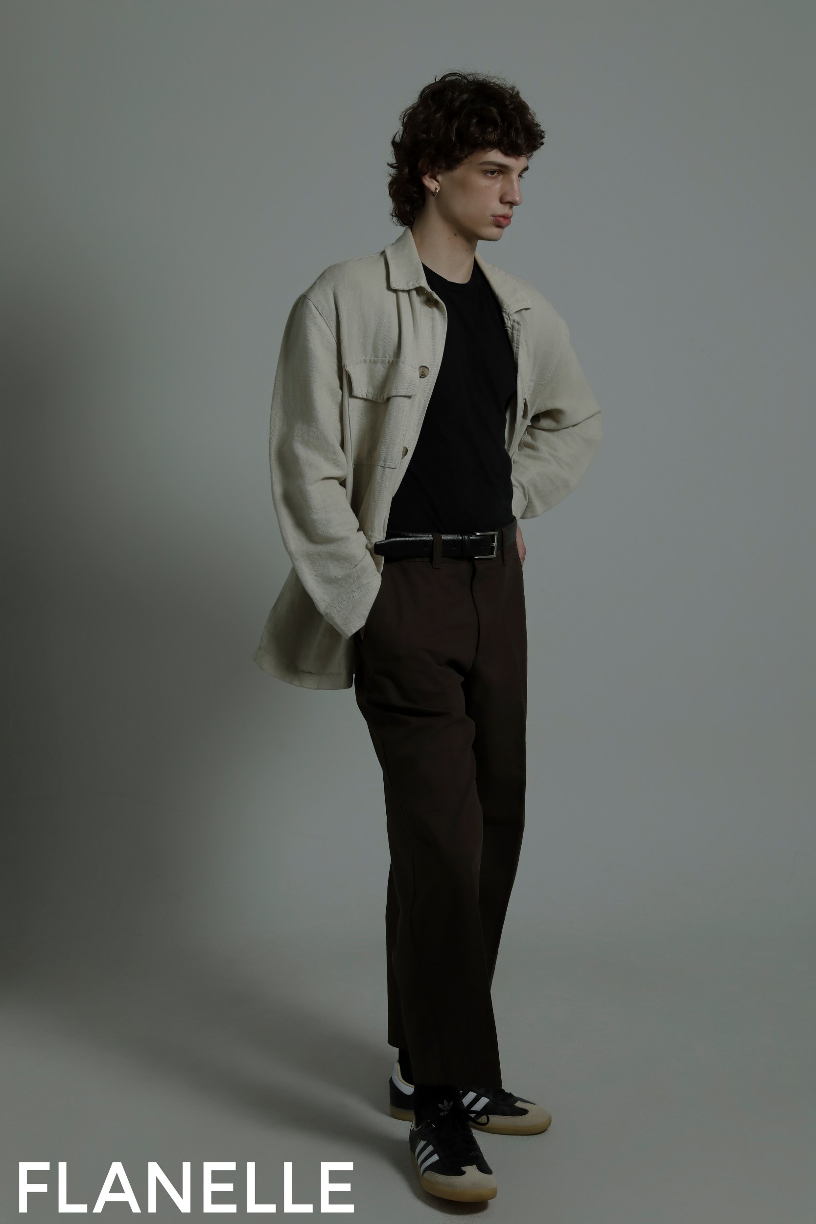 Man wearing stylish outfit with beige shirt, black tee, and brown pants. Fashion pose.