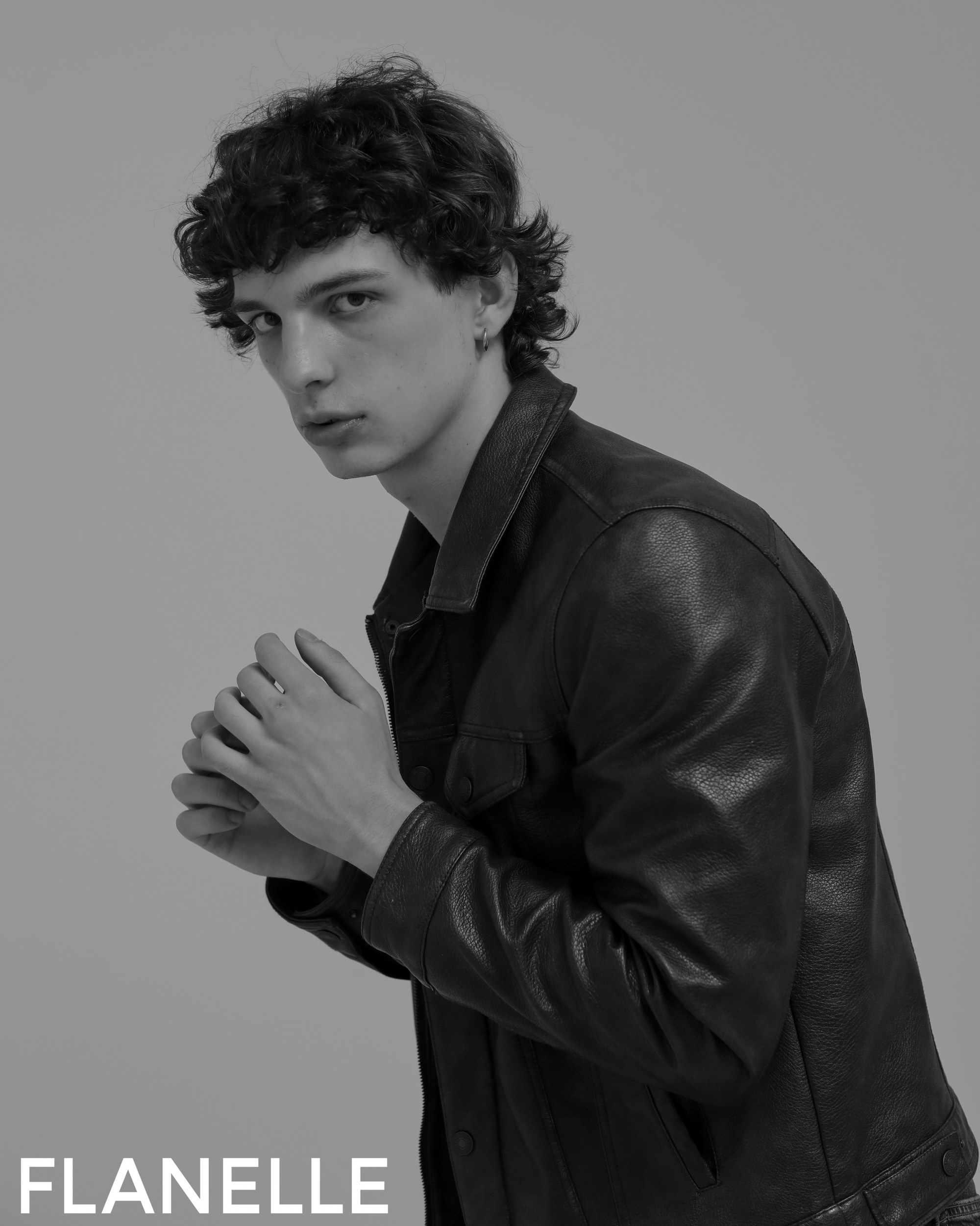 Young man in leather jacket poses thoughtfully for Flanelle fashion photoshoot.