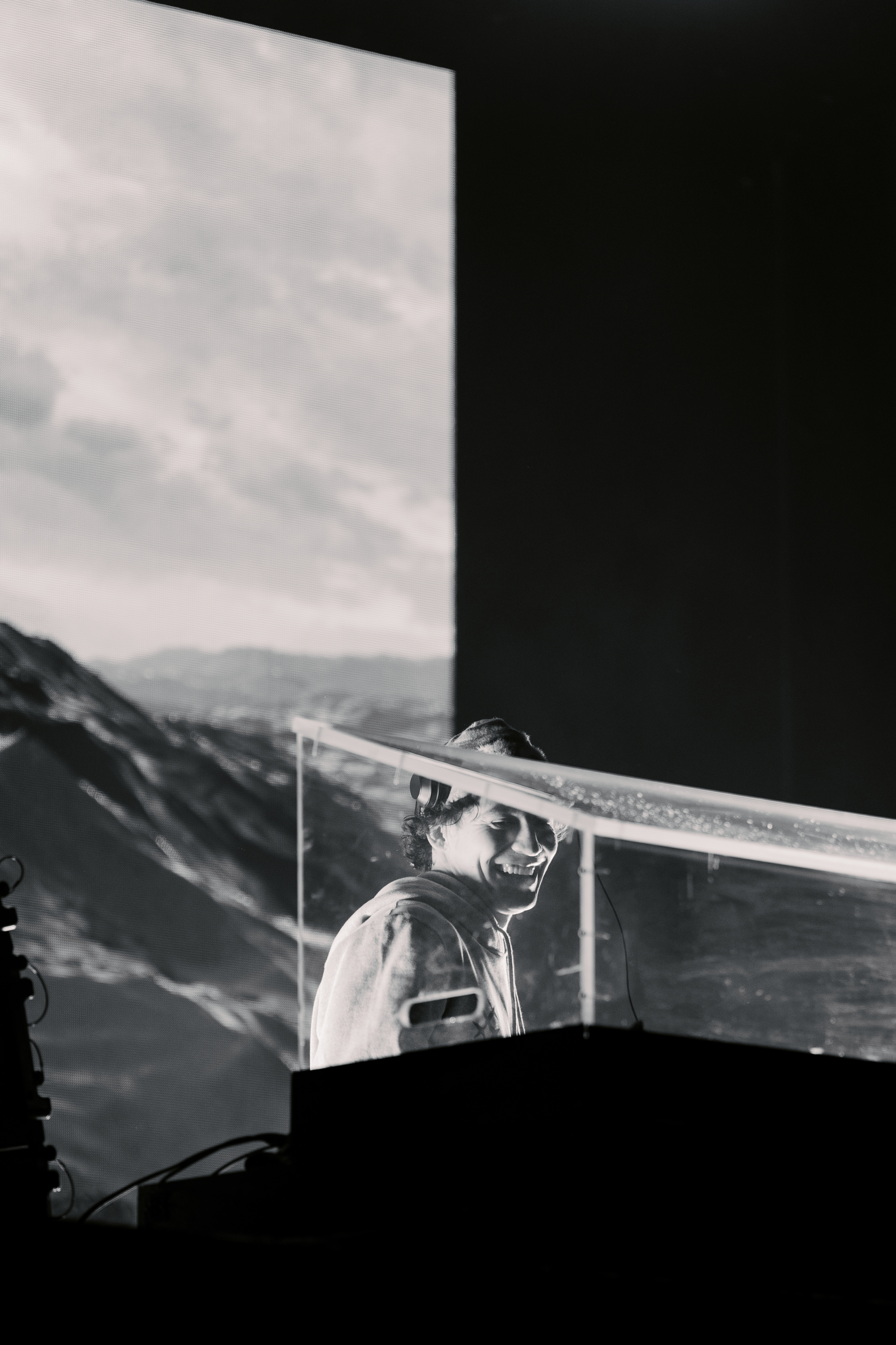 DJ performing on stage with mountain background, black and white photo.