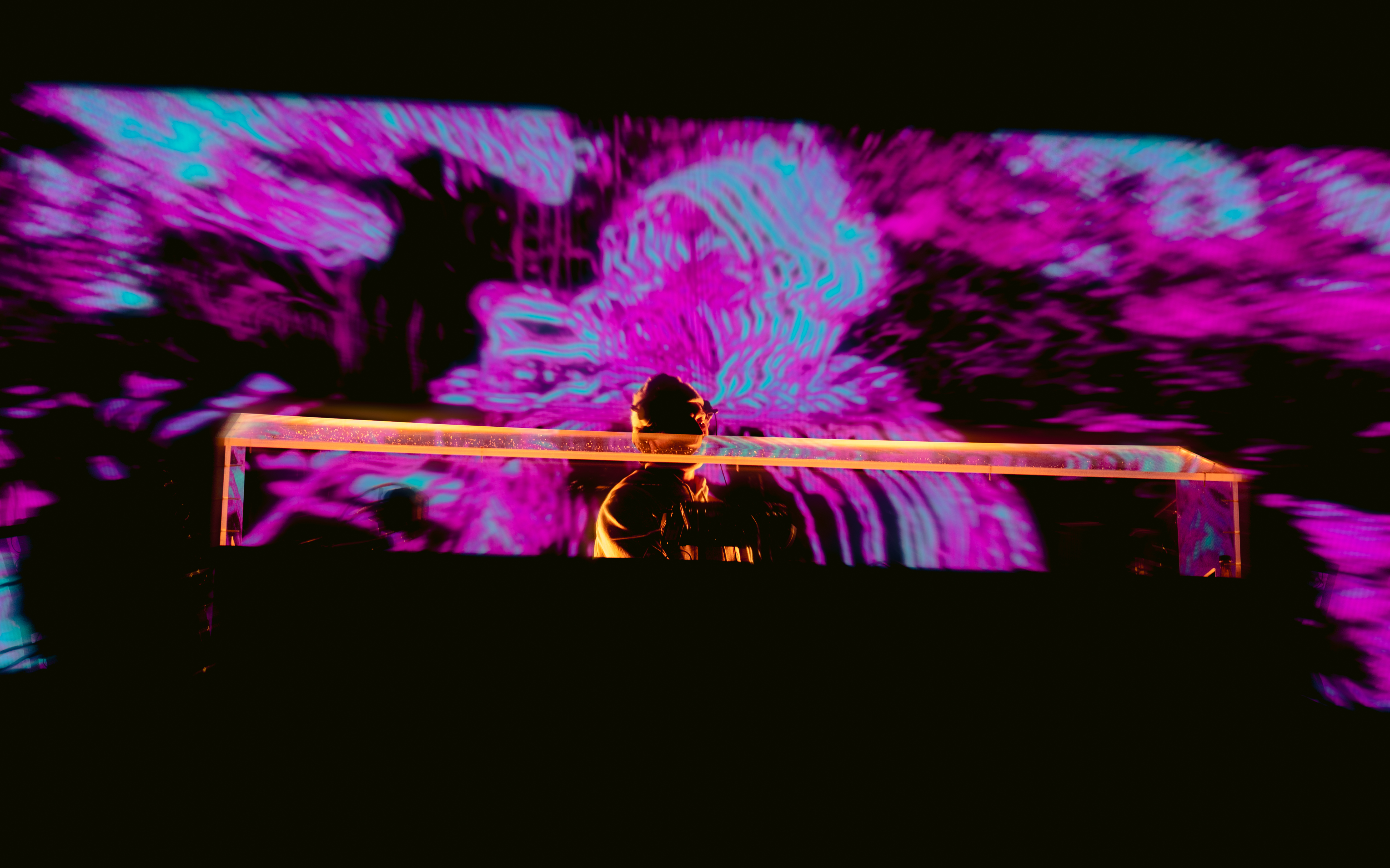 DJ performing live with vibrant purple and blue visuals in the background.