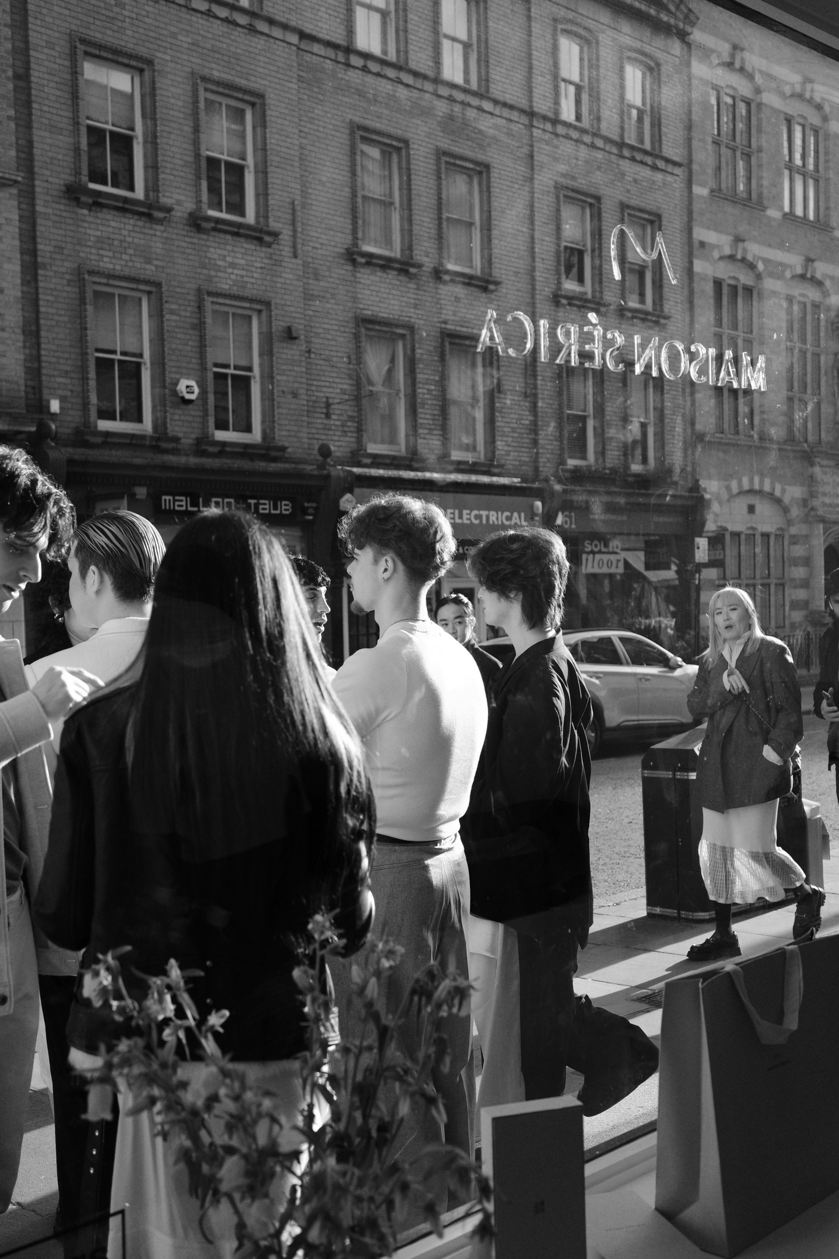 People gathered outside a store window, urban street reflection in black and white.