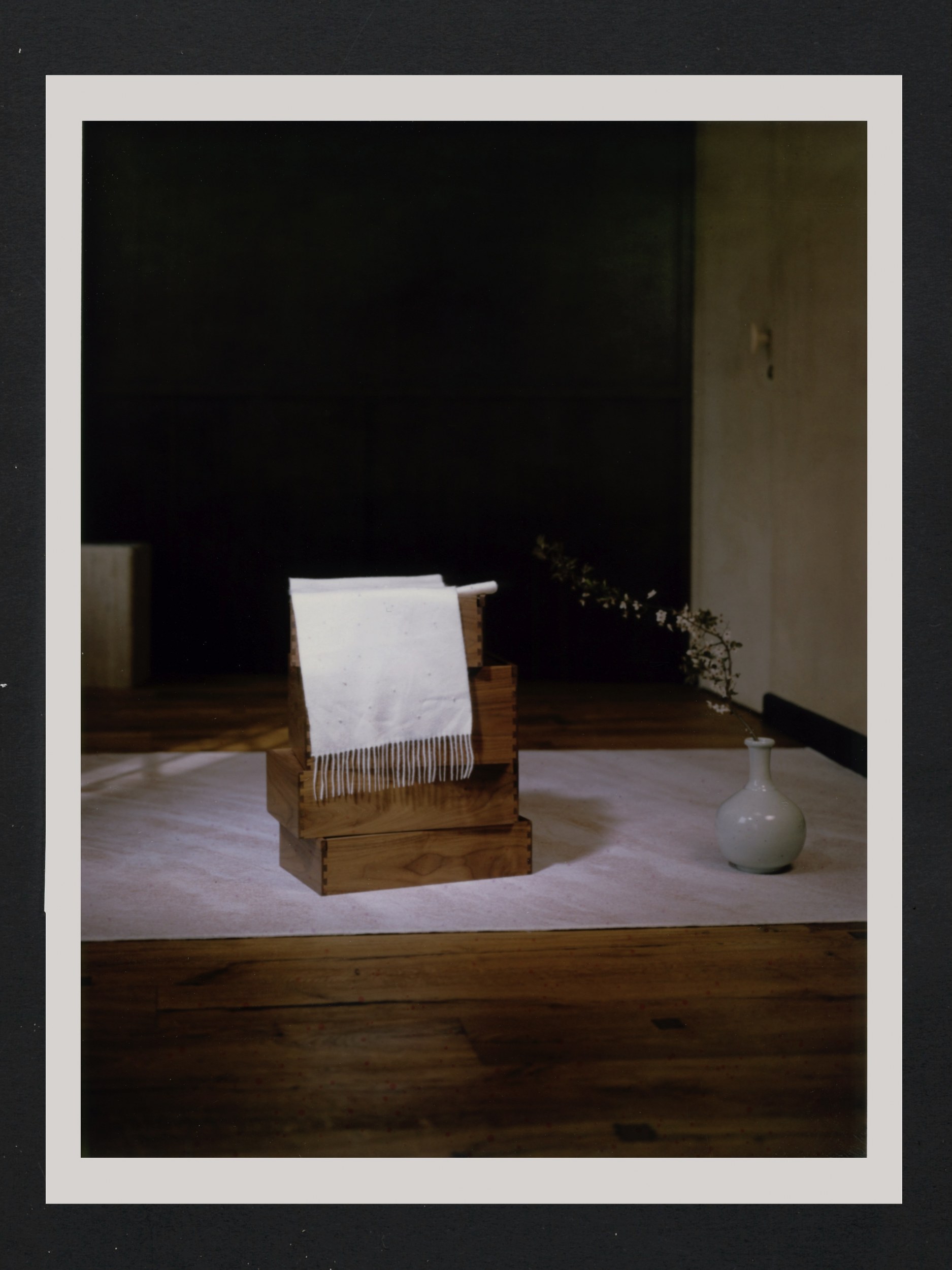 Minimalist interior with wooden blocks, white vase, and a draped fringed cloth.