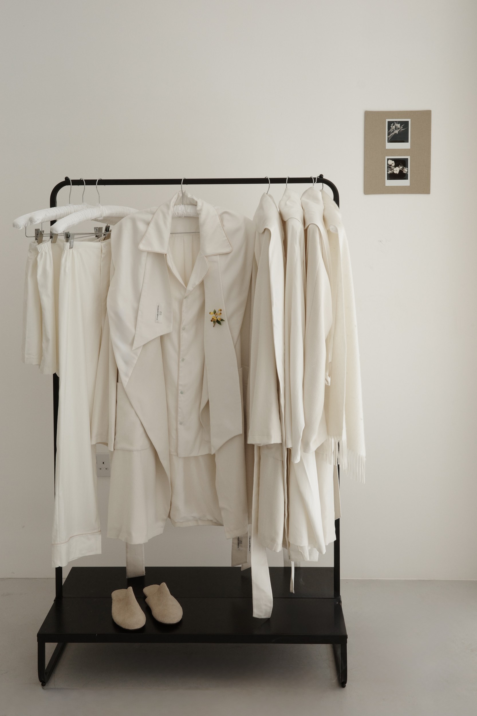 Minimalist wardrobe with white clothing and slippers on a black rack.
