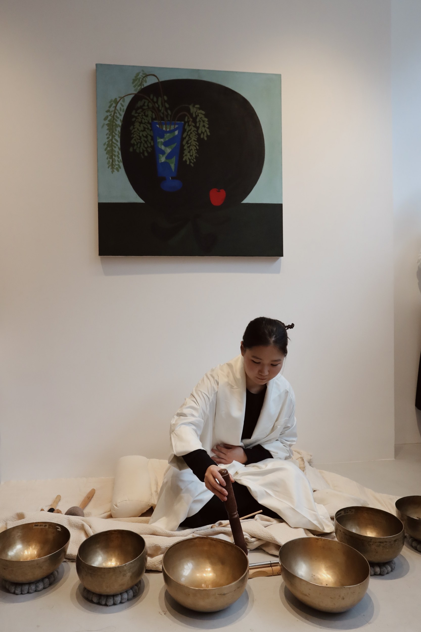 Person playing singing bowls with artwork in the background.