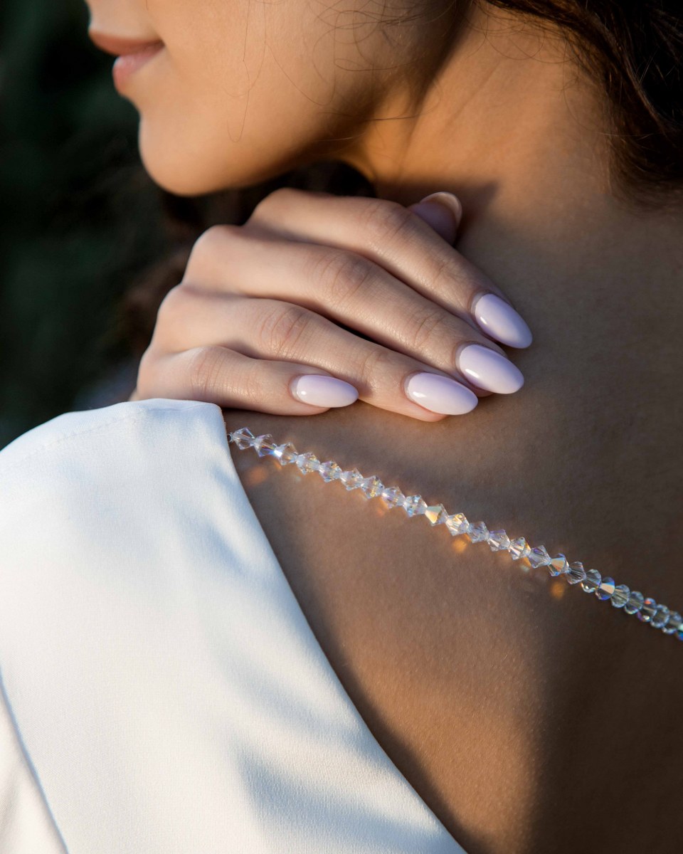 Elegant nails and sequined strap on woman's shoulder in soft lighting.
