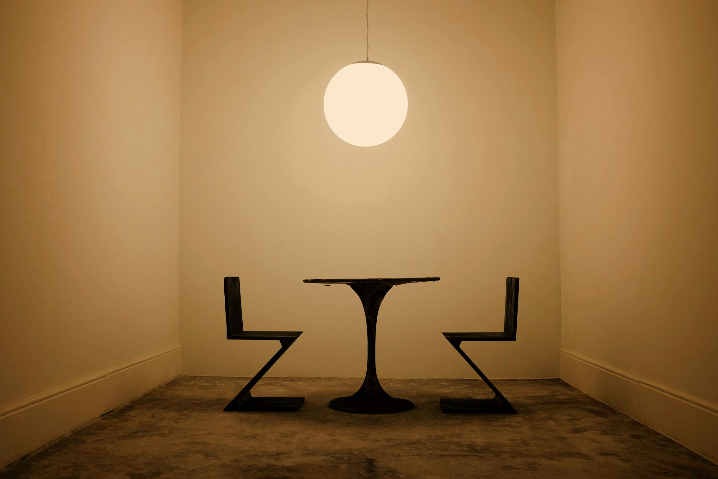 Minimalist room with geometric chairs, round table, and hanging light fixture.