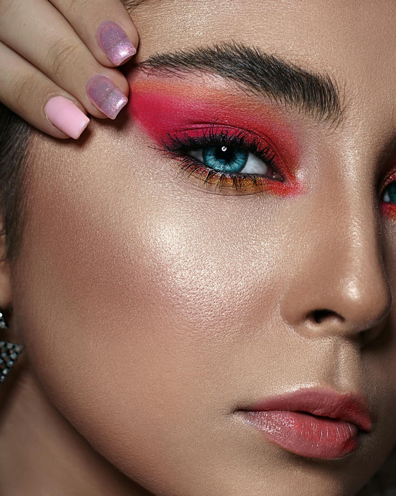Close-up of vibrant eye makeup and glossy lips with manicured pink nails.