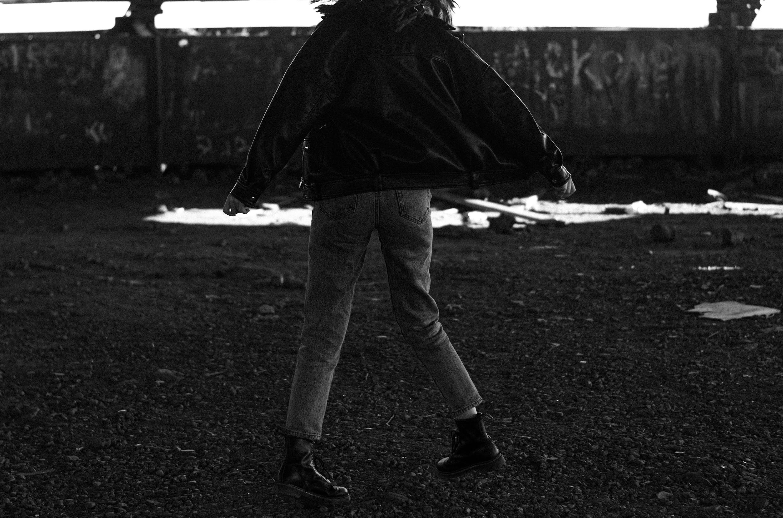 Person dancing freely in a grungy urban setting, wearing a leather jacket and jeans.