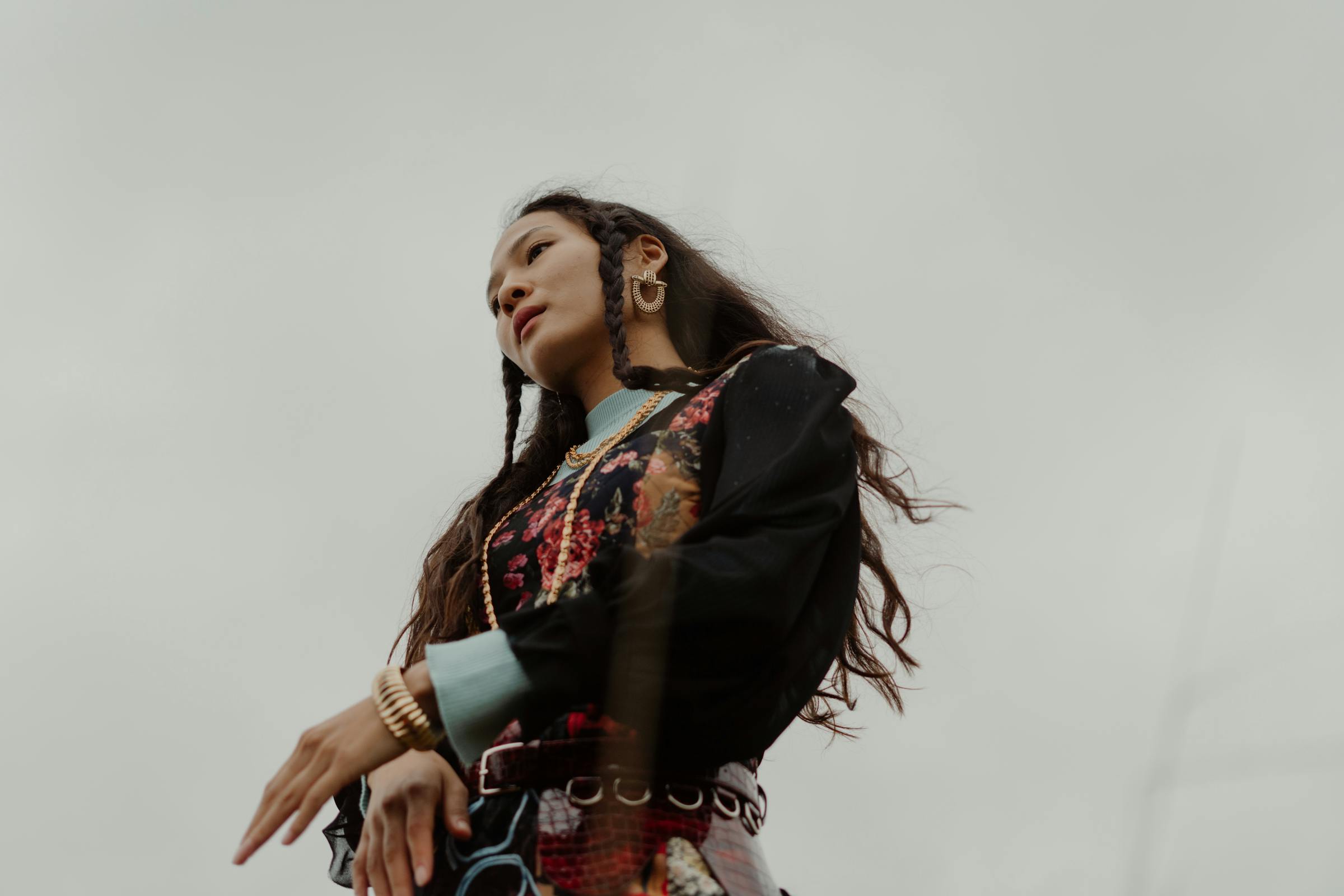 Fashionable woman with braided hair and colorful outfit against cloudy sky.