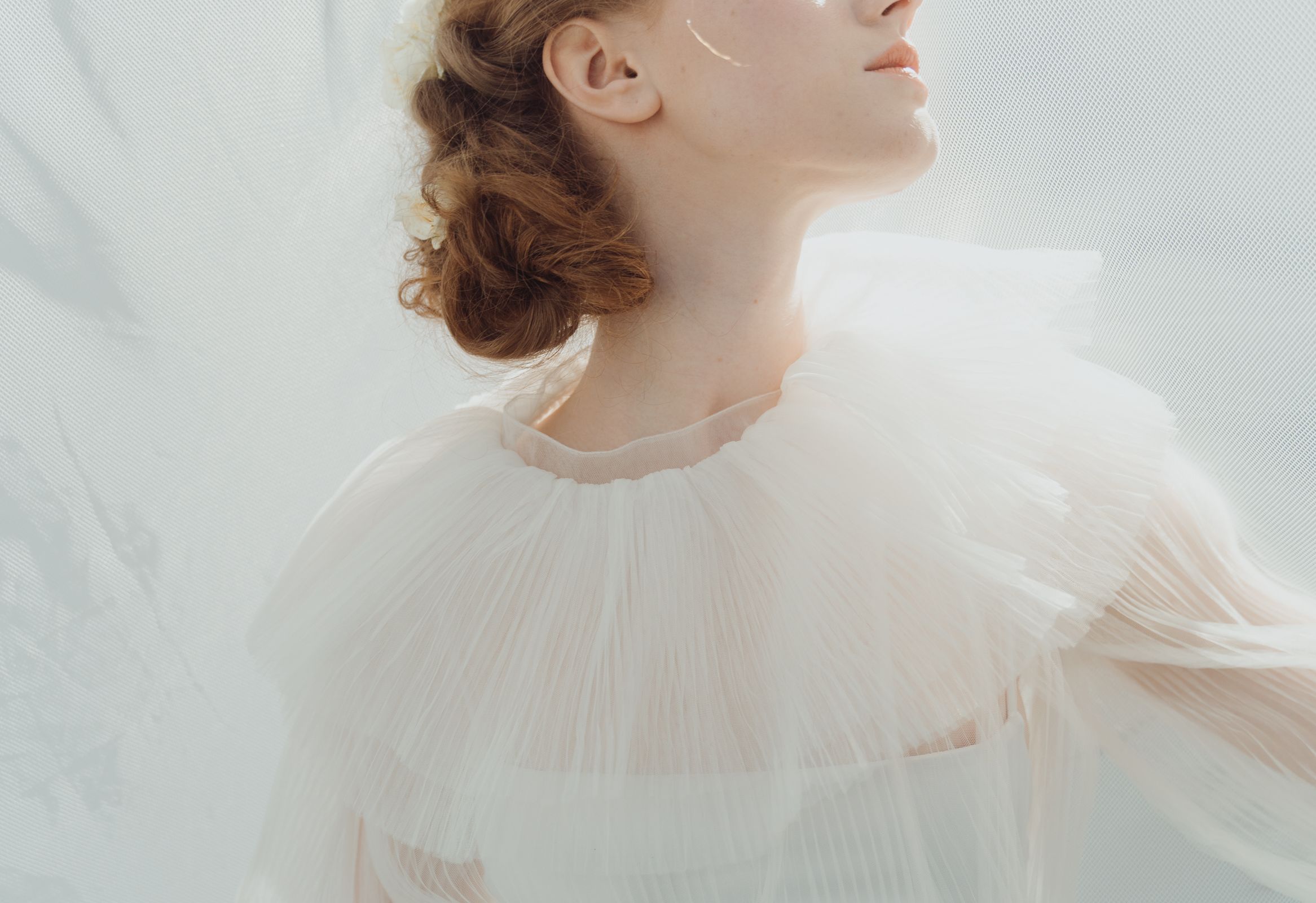 Elegant woman in sheer white dress with delicate frills, soft light background.