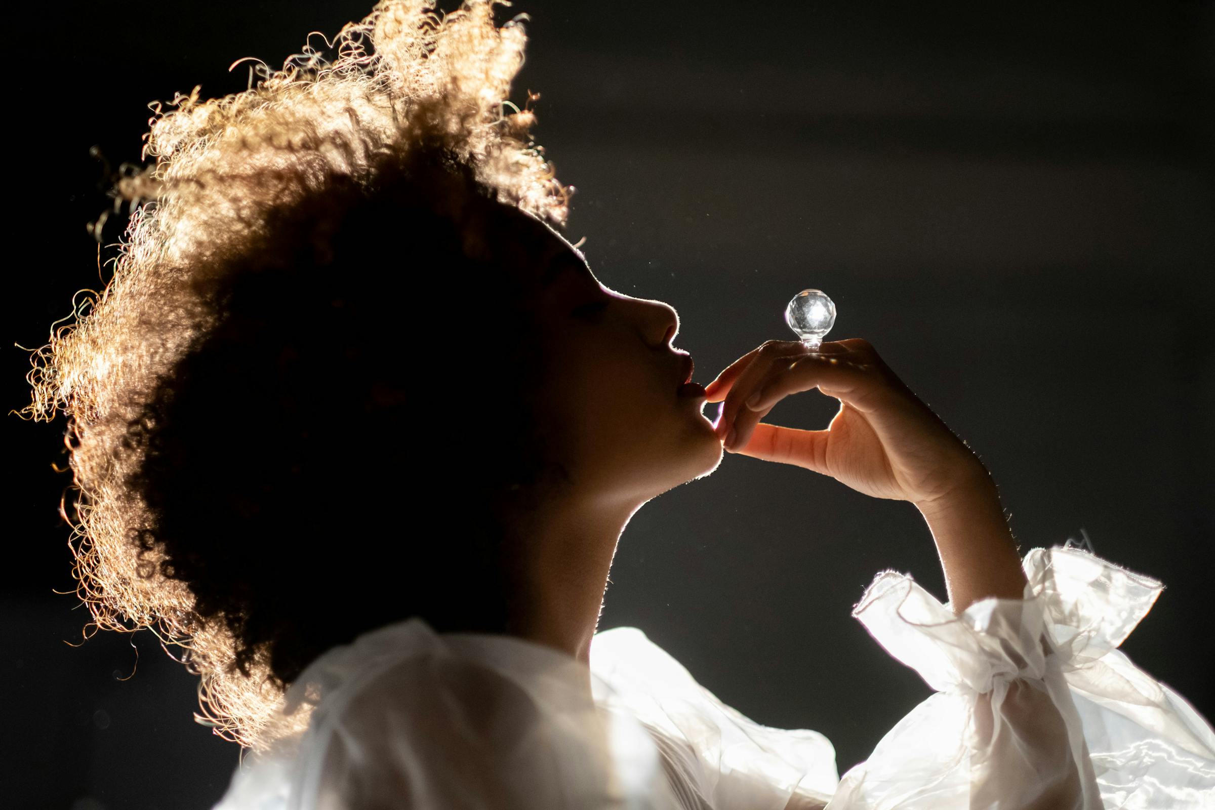 Silhouette of person with curly hair holding crystal orb against dramatic lighting.
