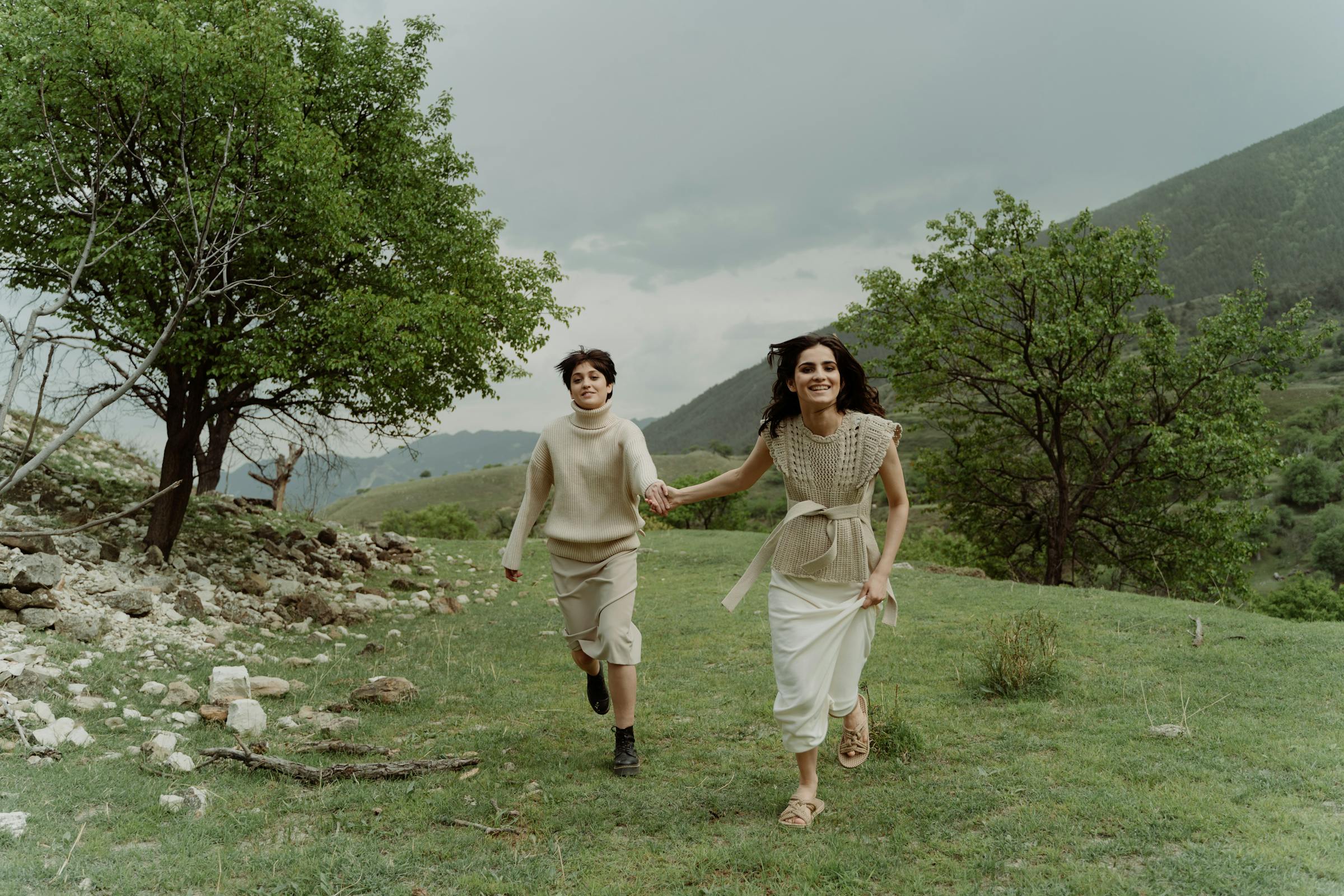 People joyfully running in a lush green landscape under a cloudy sky.