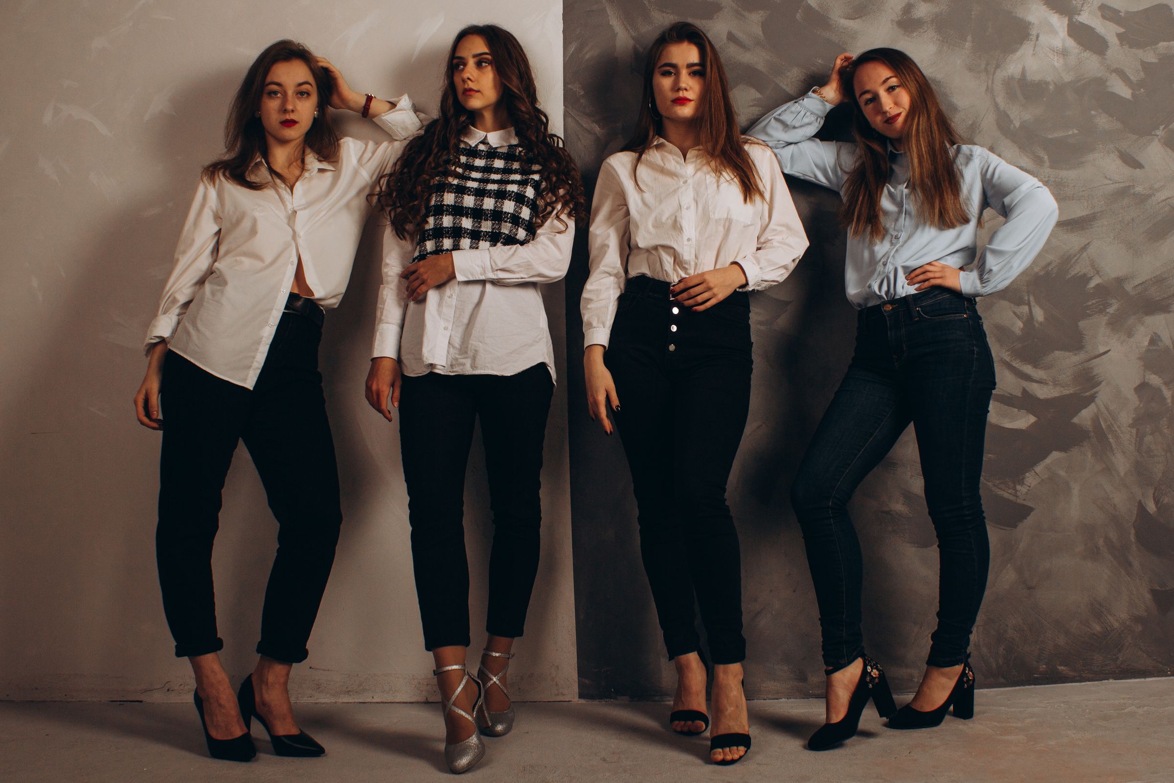 Four women pose stylishly in coordinated outfits against a textured background.