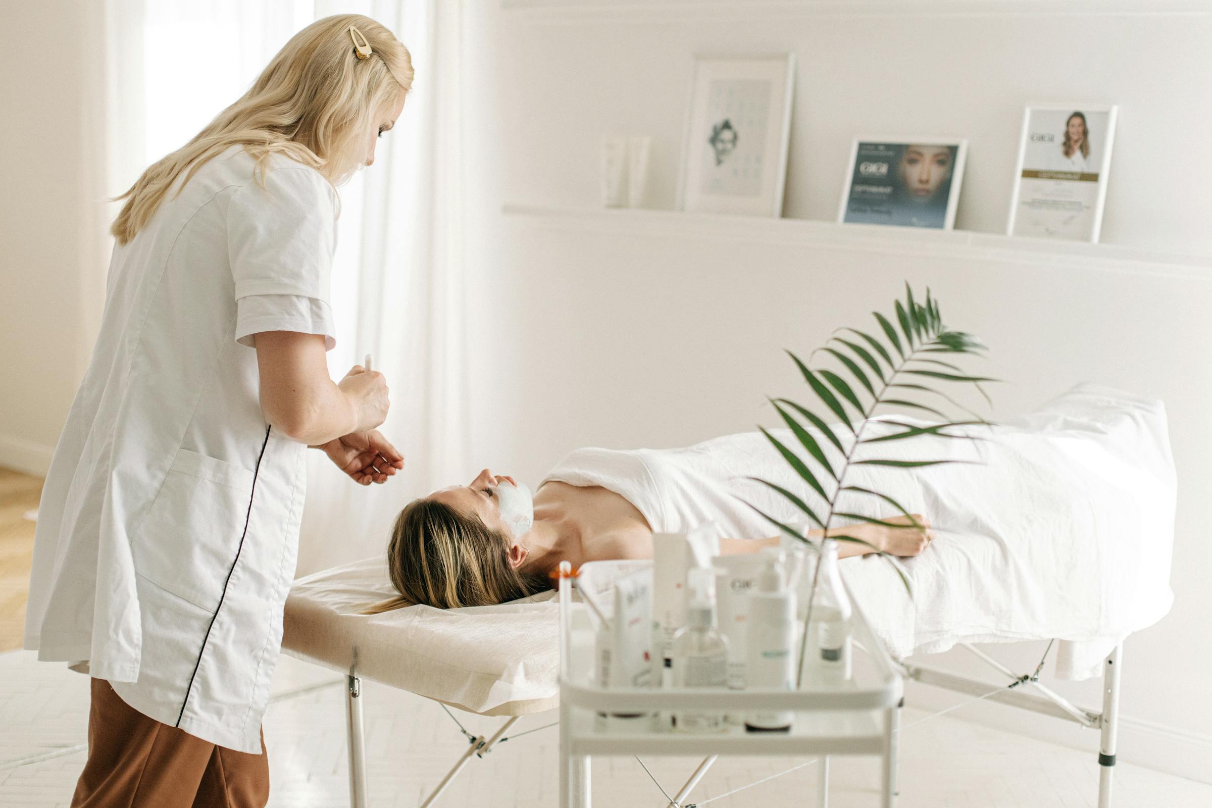 Spa facial treatment with esthetician applying mask on client. Relaxing session setup.