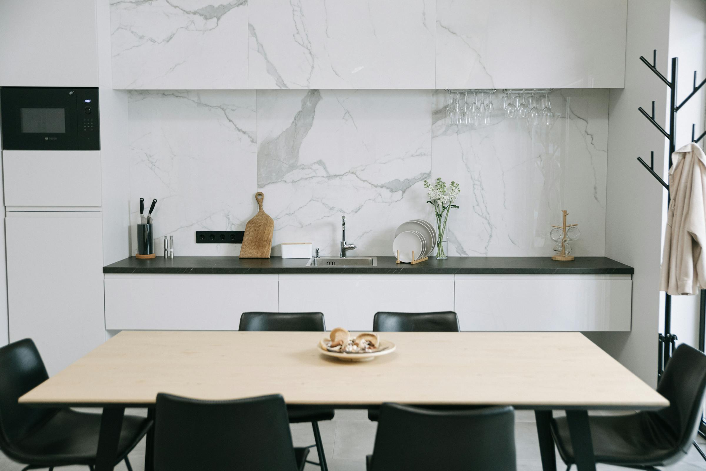 Modern kitchen with marble backsplash, wooden table, and sleek black chairs.
