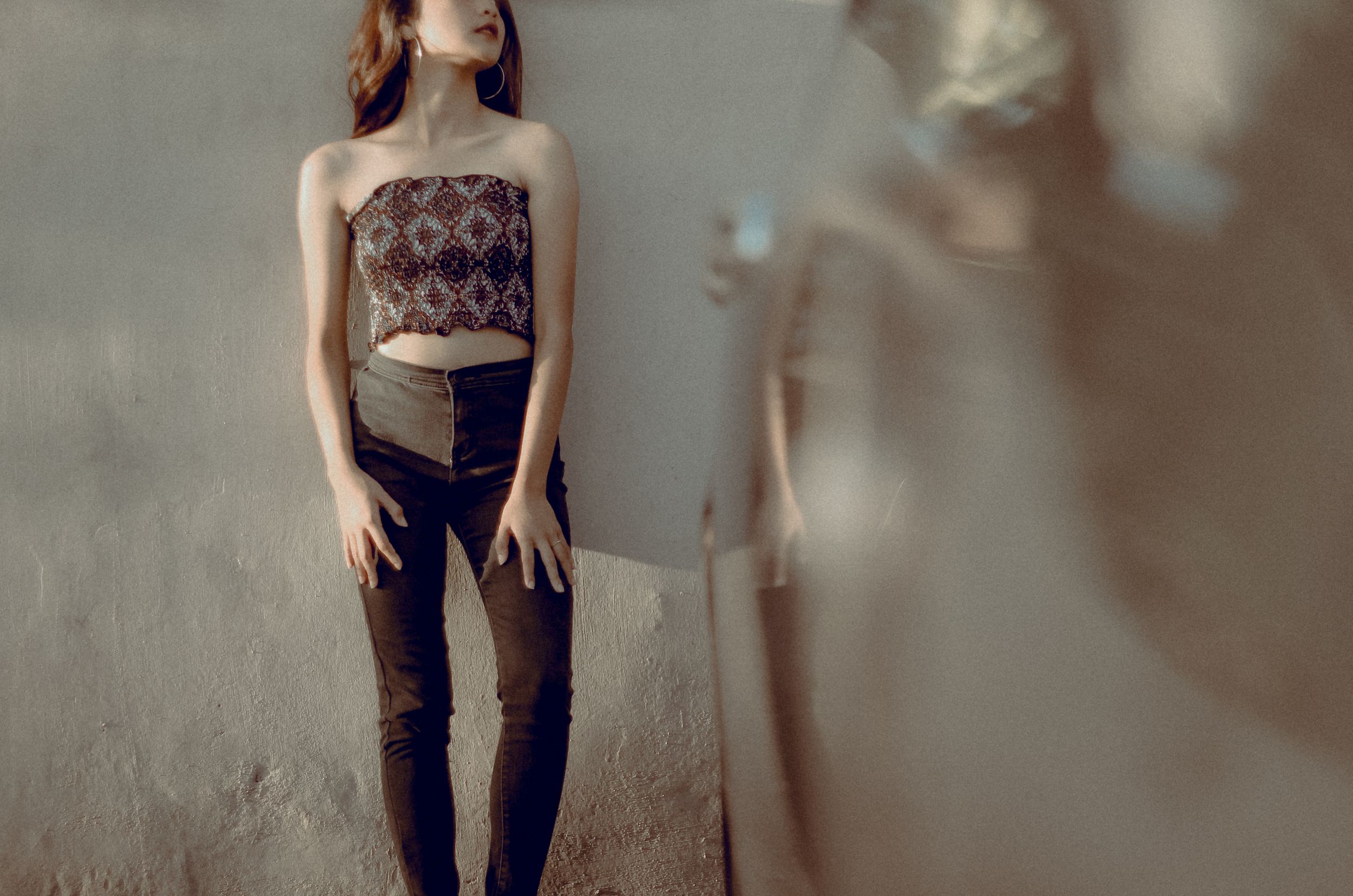 Woman in patterned top and jeans stands against beige wall. Fashion style concept.