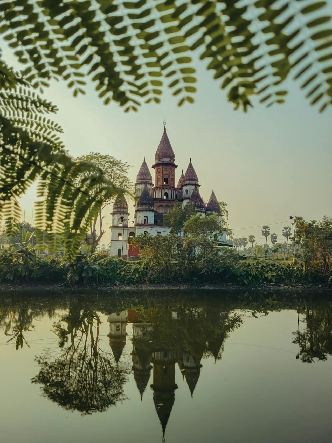 Temple with spires reflected in a tranquil pond, framed by lush greenery.
