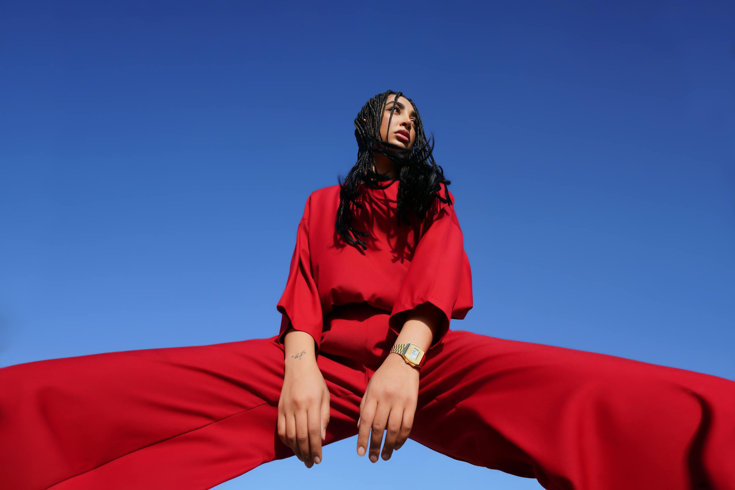 Person in red outfit against blue sky, standing in a powerful pose, low-angle view.
