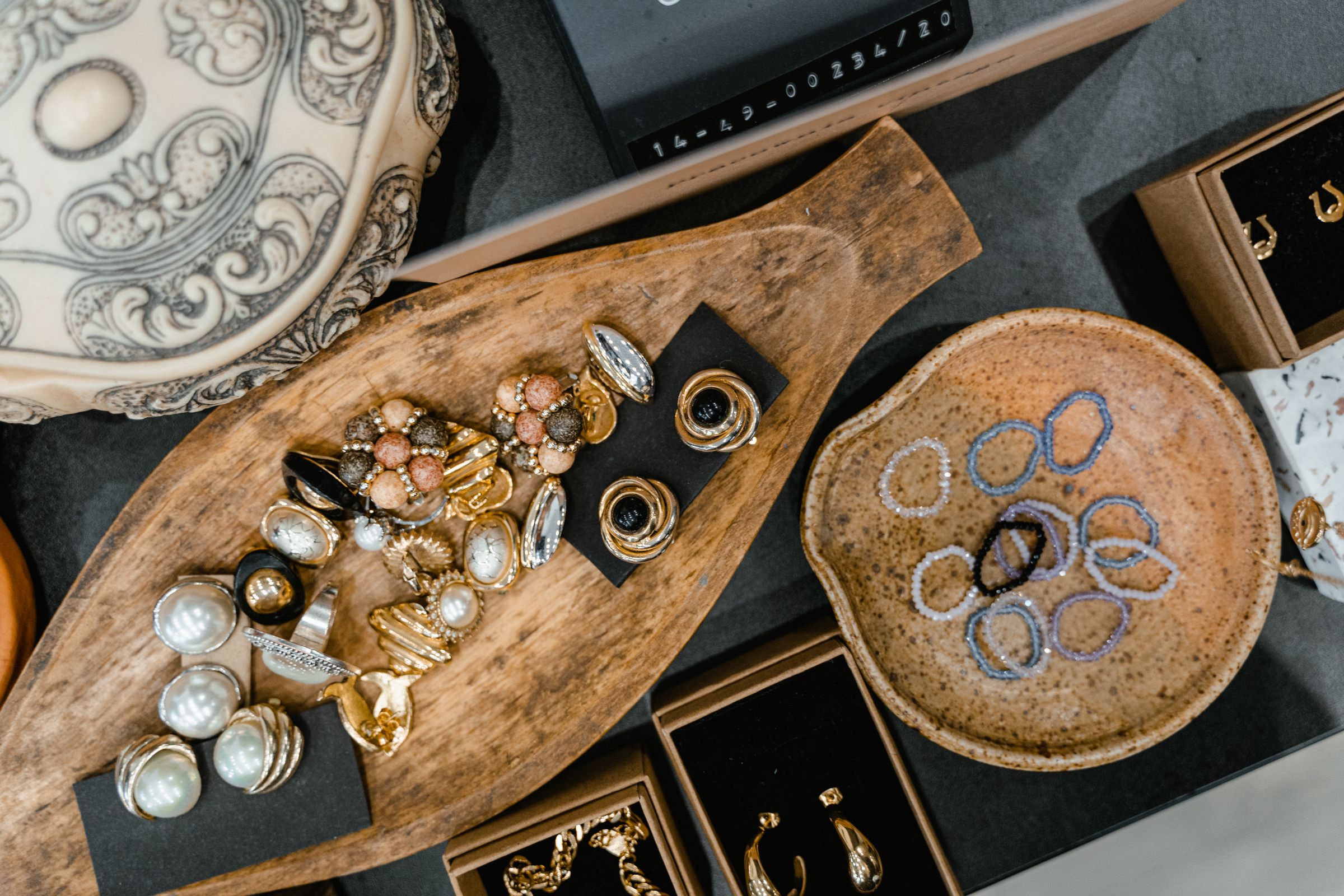 Assorted jewelry displayed on decorative wooden and ceramic trays.