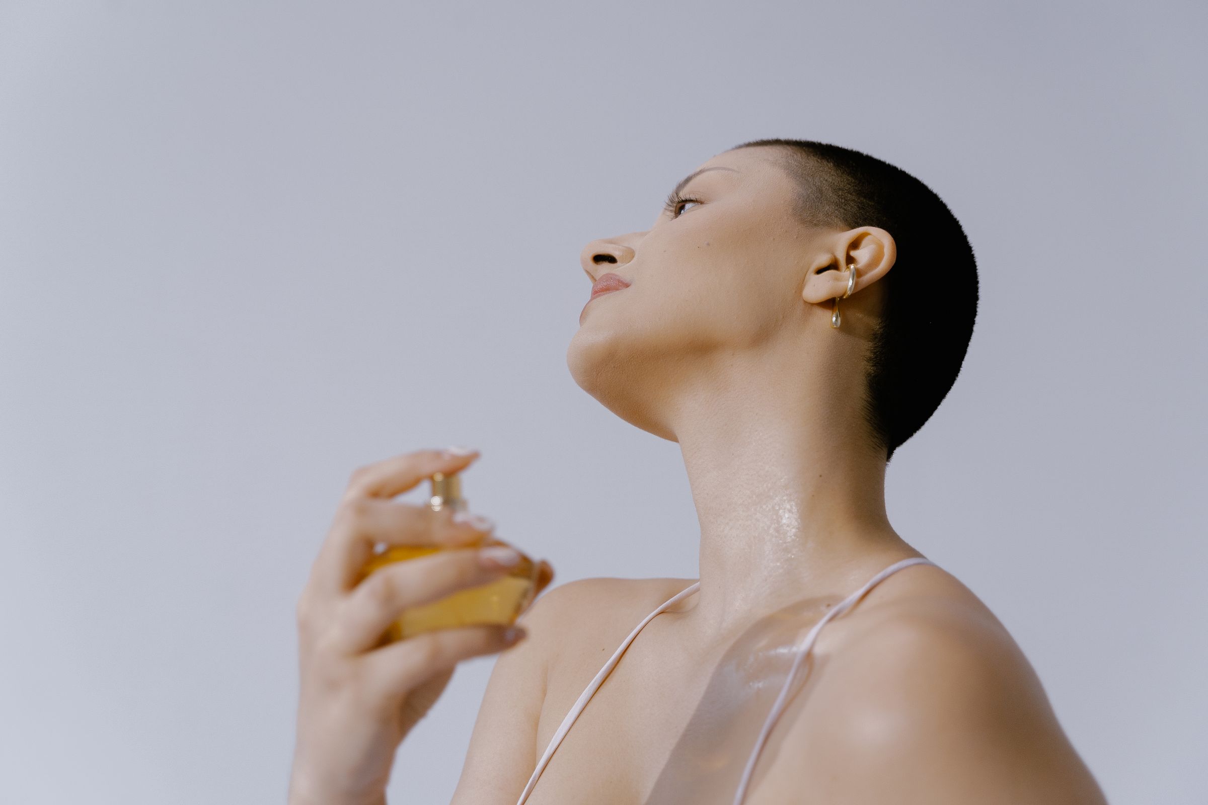 Person applying perfume on neck with a spray bottle, elegant fragrance concept.