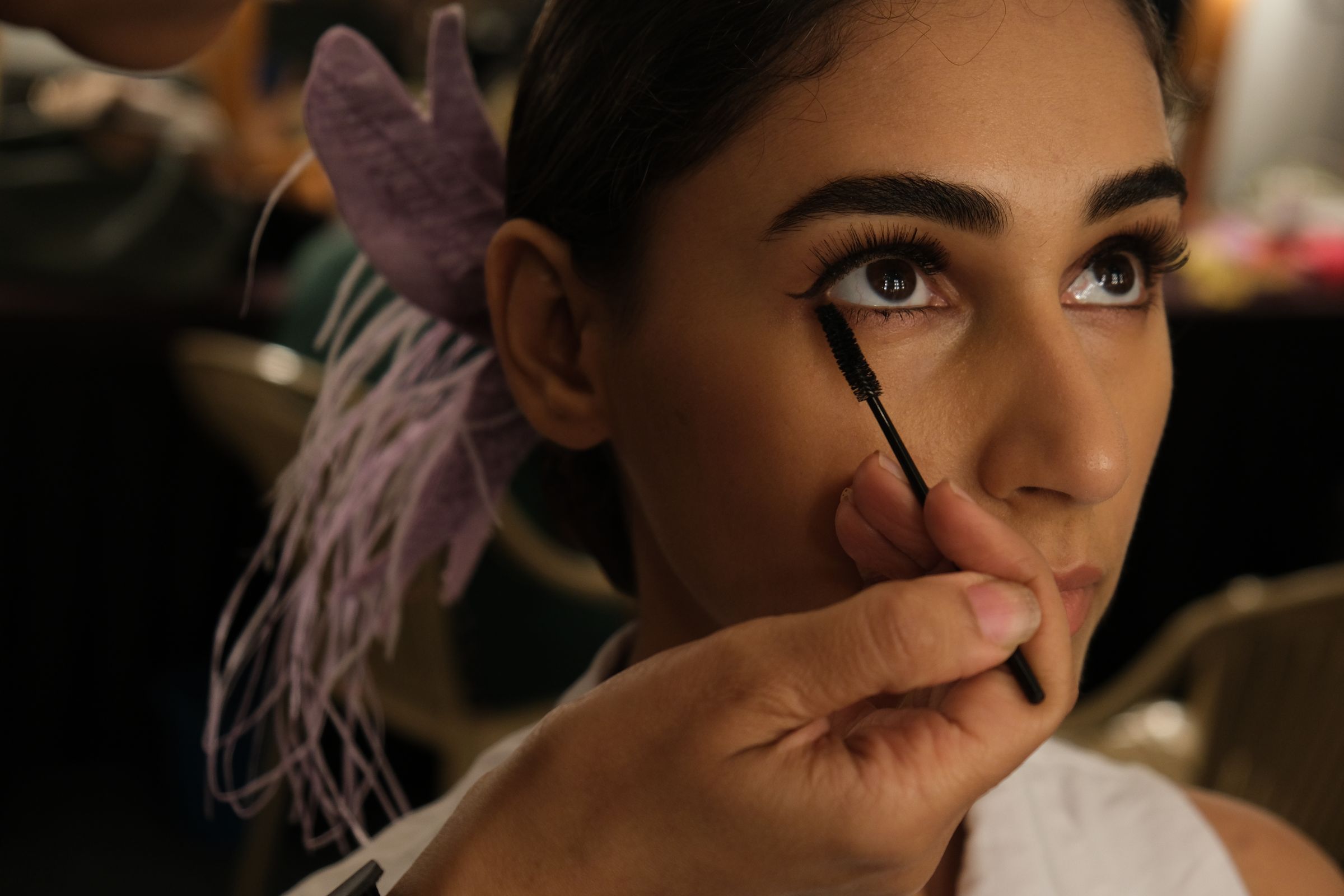 Woman applying mascara, makeup artist prepares for event backstage.