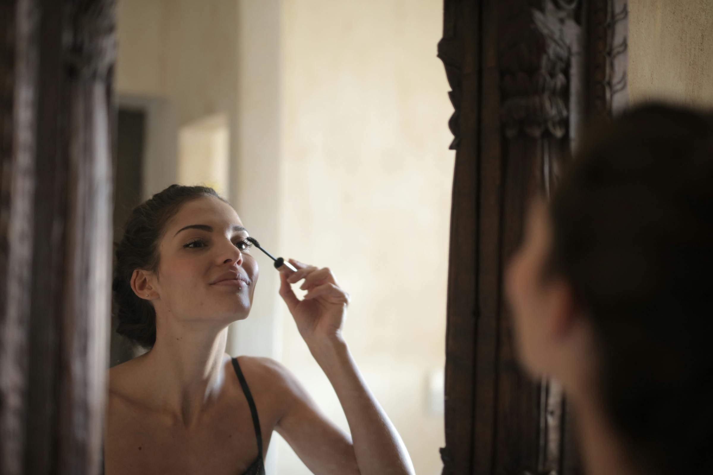 Woman applying mascara in front of a mirror, enhancing her eyelashes.
