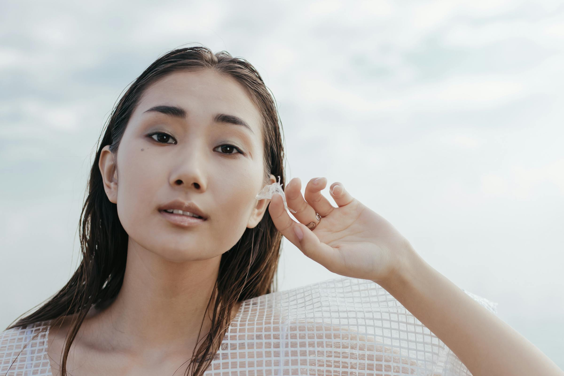 Close-up of a woman holding a flower petal by her face, wearing a netted top.