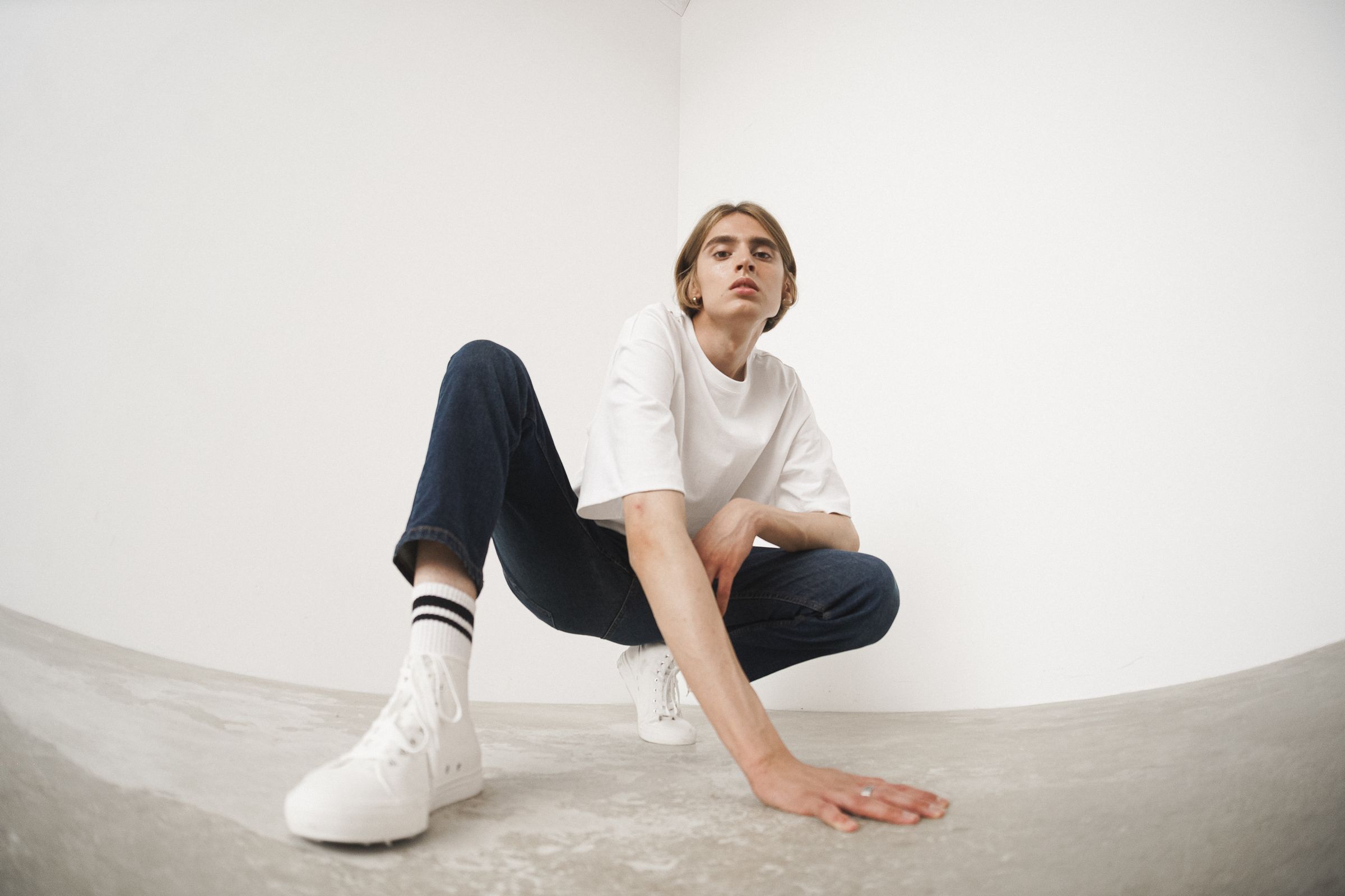 Person in casual white shirt and jeans posing in a minimalist space.