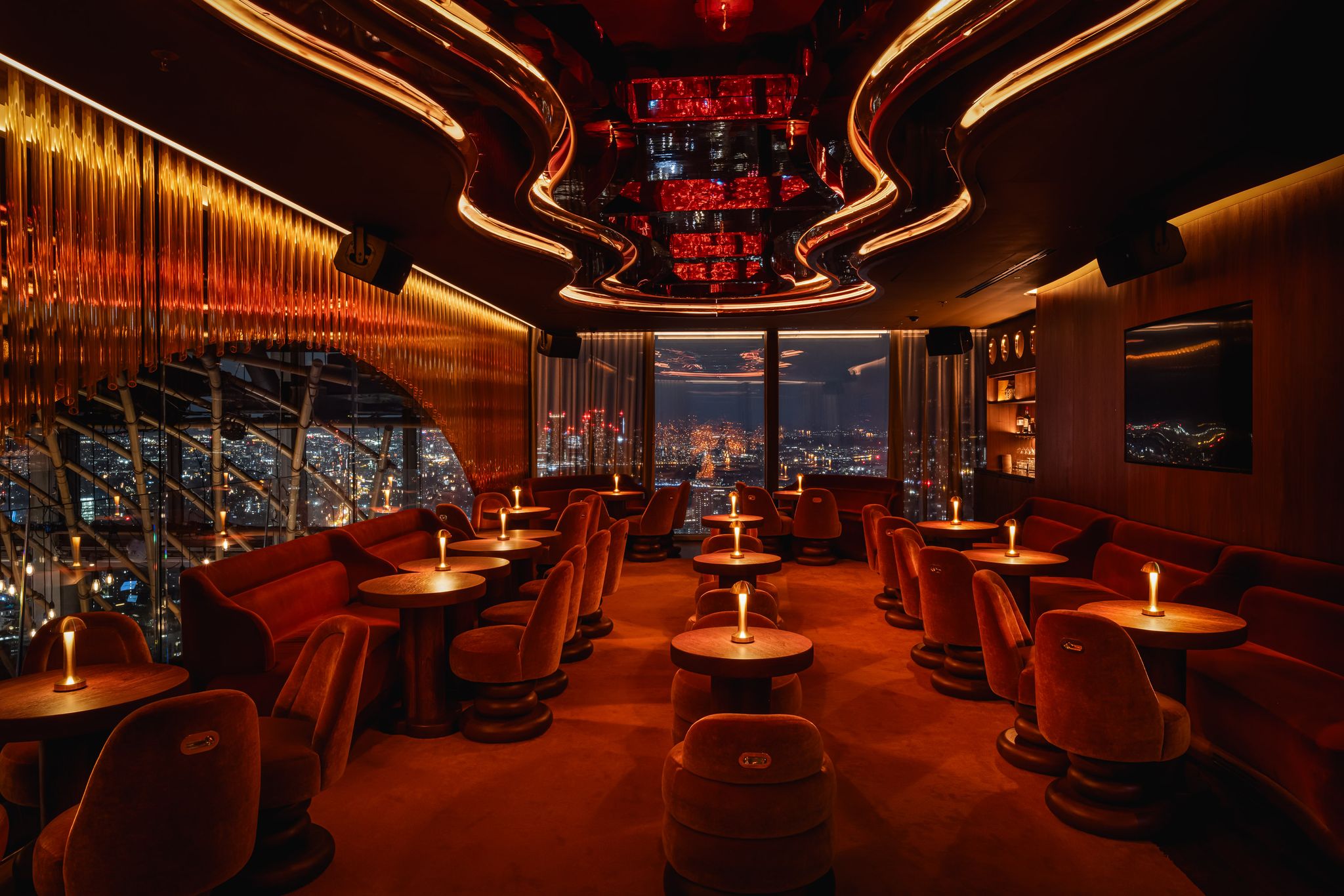 Luxurious city view lounge with ambient lighting and red velvet seating.