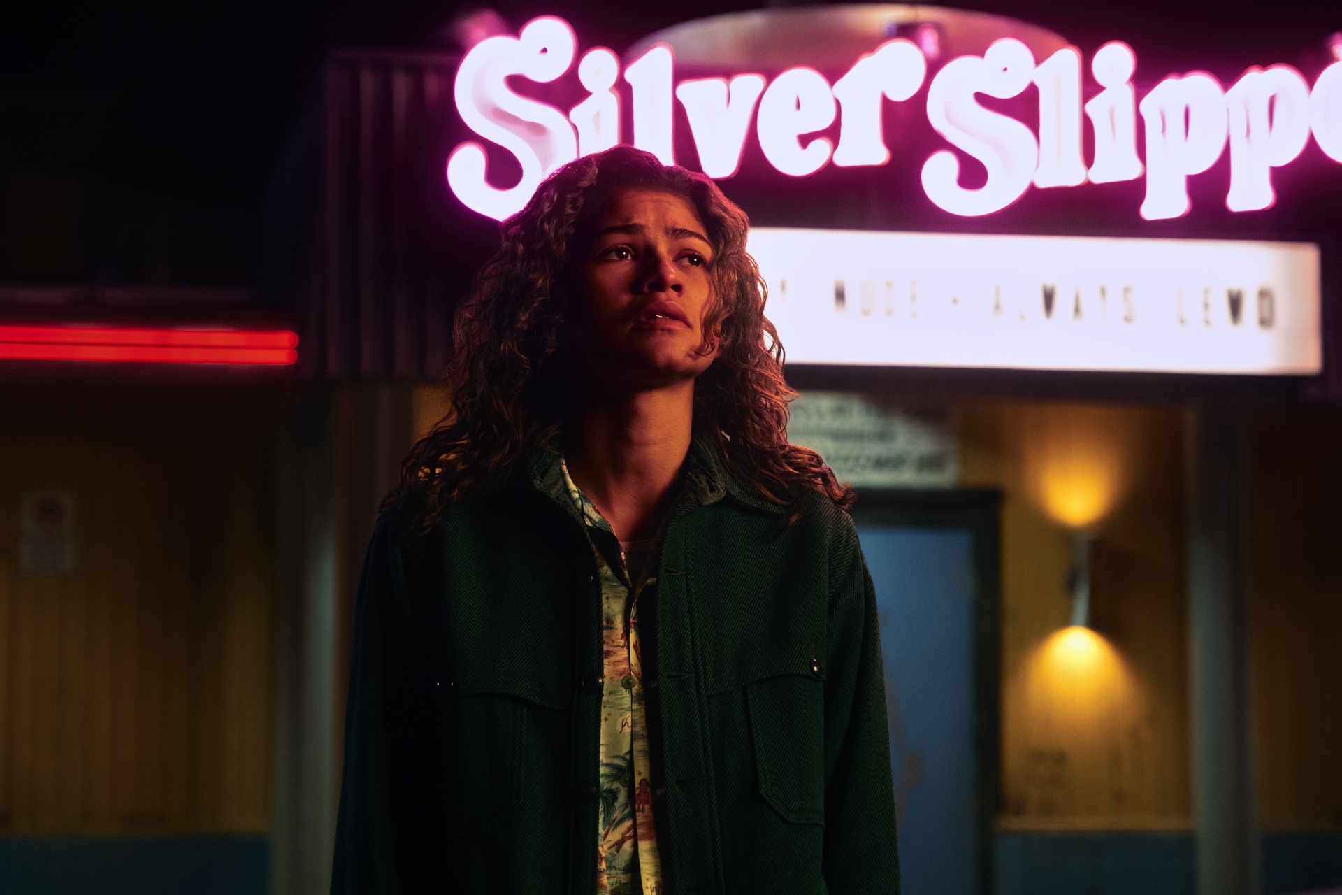 Person standing under neon Silver Slipper sign at night, wearing a dark jacket.